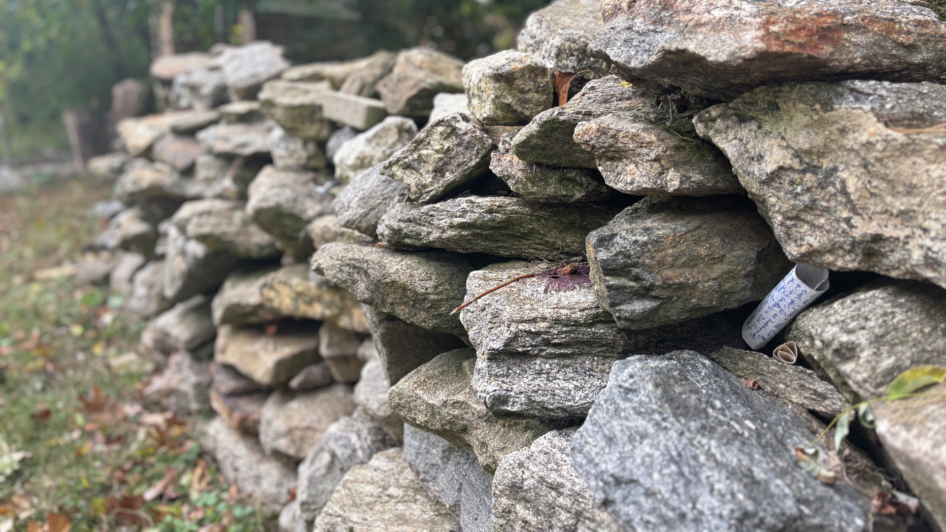 A dry stacked rock wall contains notes to loved ones as a way to express and process grief