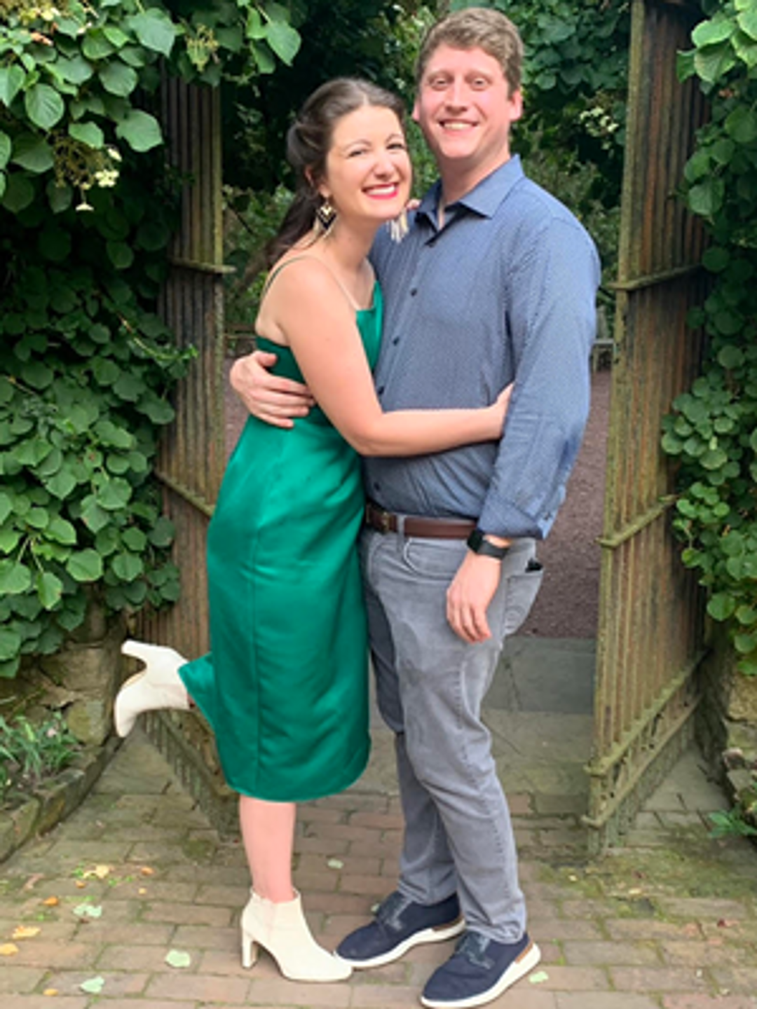 Hannah Parke hugs a man in a blue shirt, both smiling, standing in a garden with greenery.