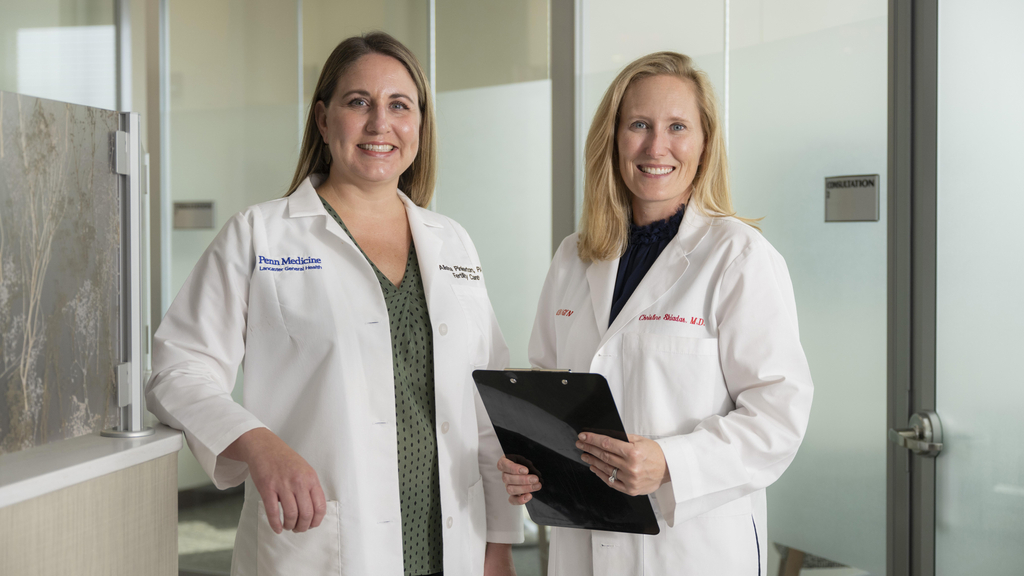 Alisha Pinkerton, PA-C a physician assistant at Penn Fertility Care Lancaster, and Christine Skiadas, MD, both in white lab coats, stand next to each other in an office setting and smile for a photo.