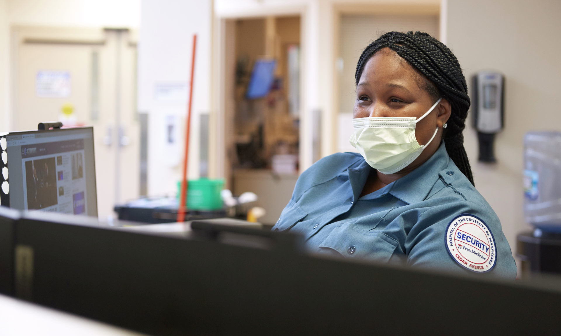 A Black female security guard has a smiling expression behind a surgical mask