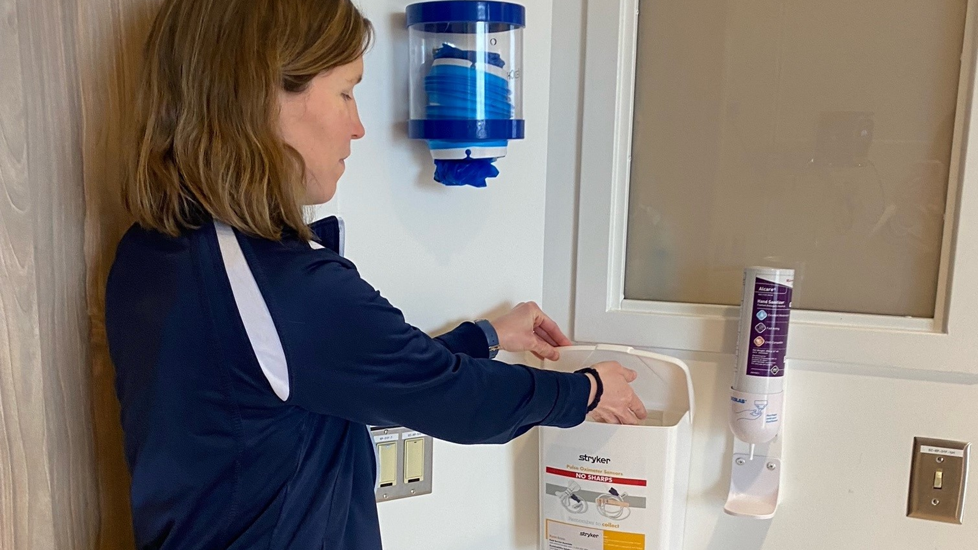 An LGH nurse demonstrates the use of a collection bin for pulse oximeters that can be refurbished by the manufacturer instead of thrown away after a single use