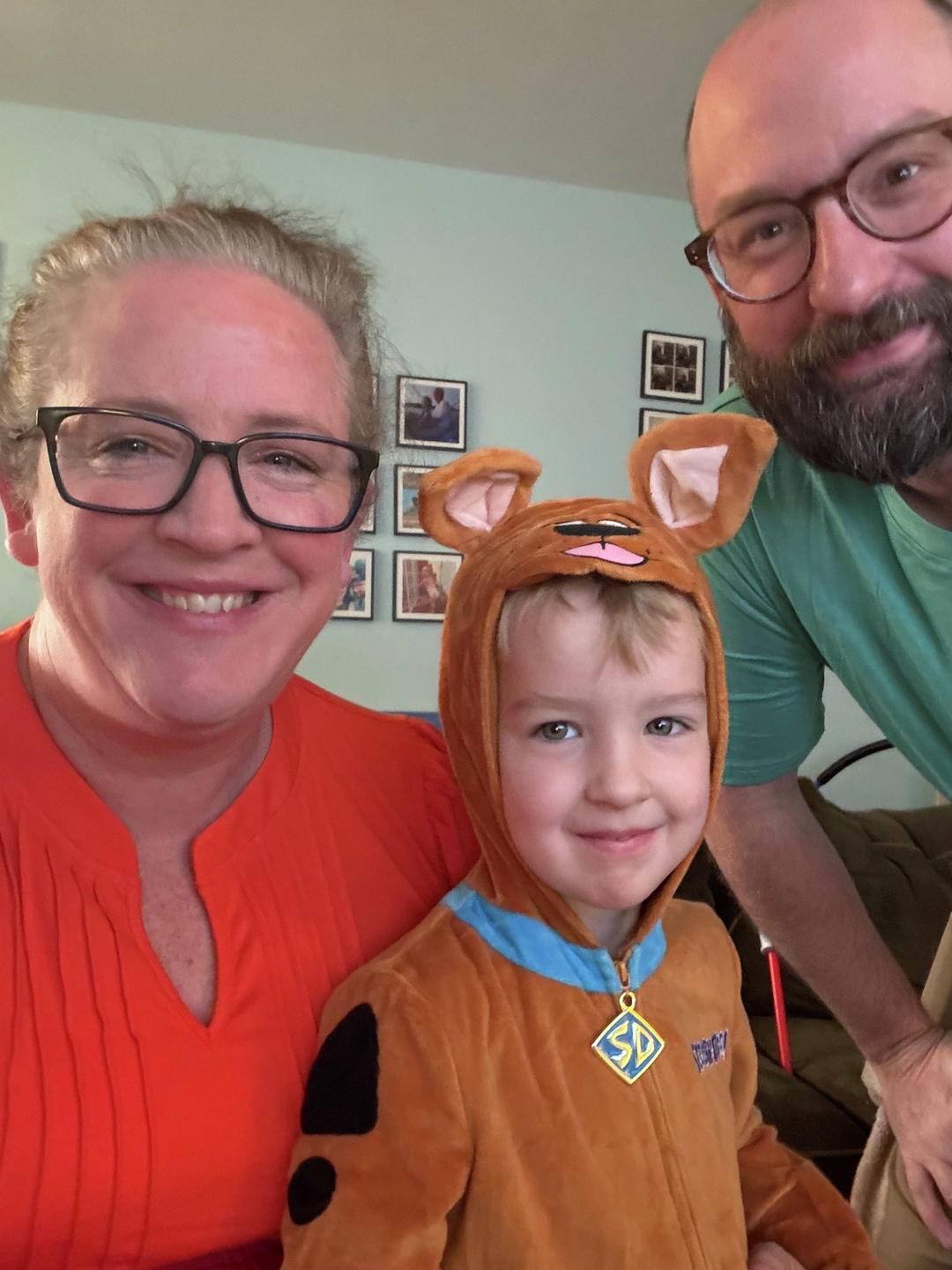 Family photo at home of Lyssa, Eric, and Ezra, who is dressed in a Scooby Doo costume