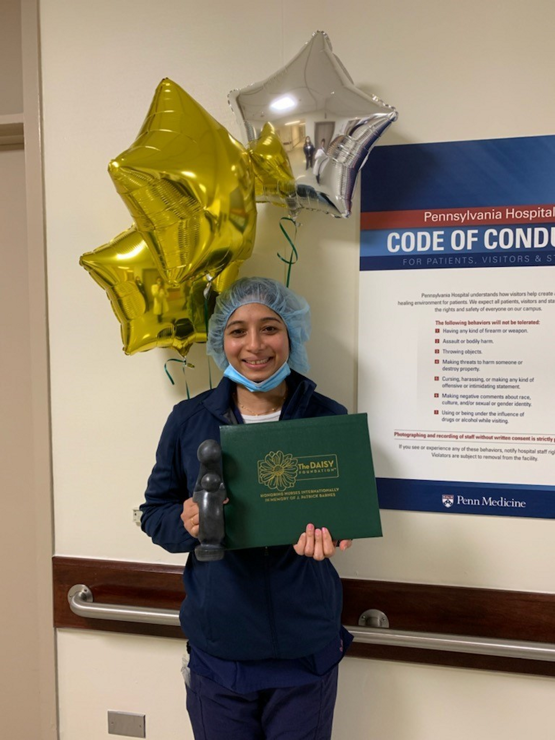 Abheena Jacob, wearing a surgical cap and holding a statue and certificate of a Daisy Award