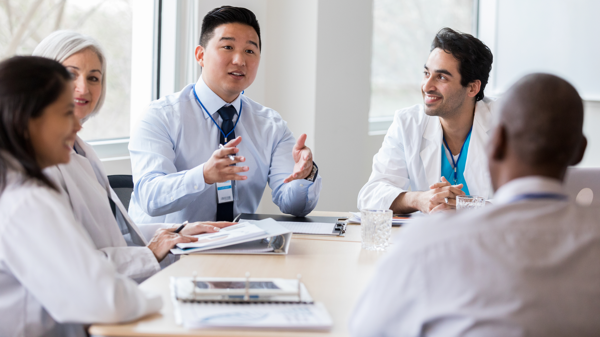 Young male hospital administrator gestures while discussing a topic with doctors 