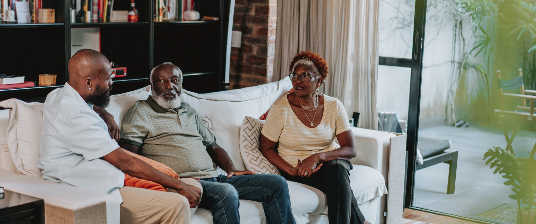 Two older parents sitting with their adult child on a couch in a living room having a discussion. 