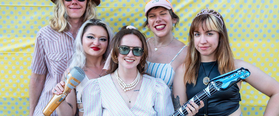 Klauser, wearing a pink baseball cap with orange cat ears, in a group shot with her band