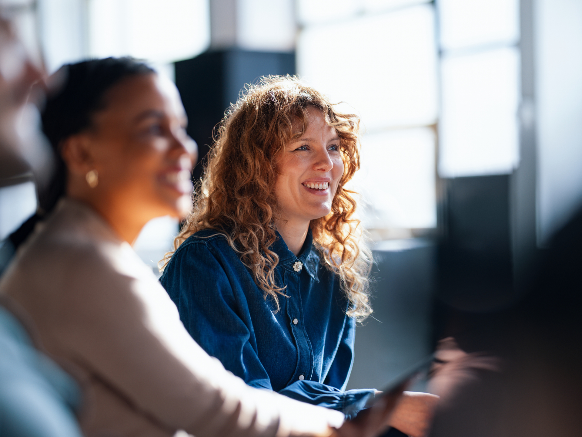 Two cheerful coworkers share ideas in a vibrant office setting, fostering a positive and collaborative workplace atmosphere.
