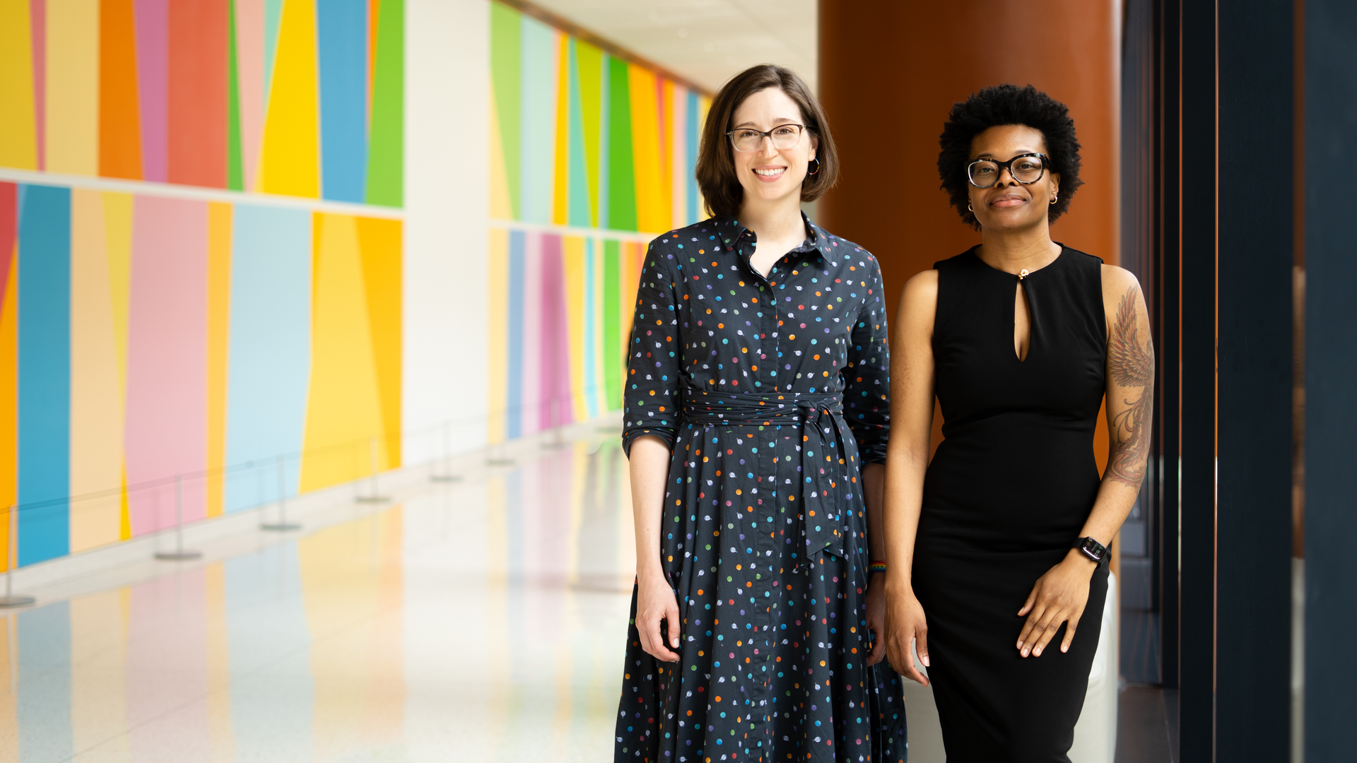 Katie Dalke, MD, and Dovie Watson, MD, stand side-by-side in the lobby of the Clifton Center near a multi-colored mural