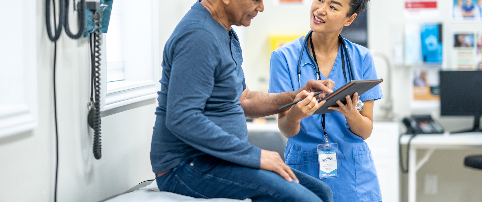 An older patient sits on an exam table during a check-up with nurse