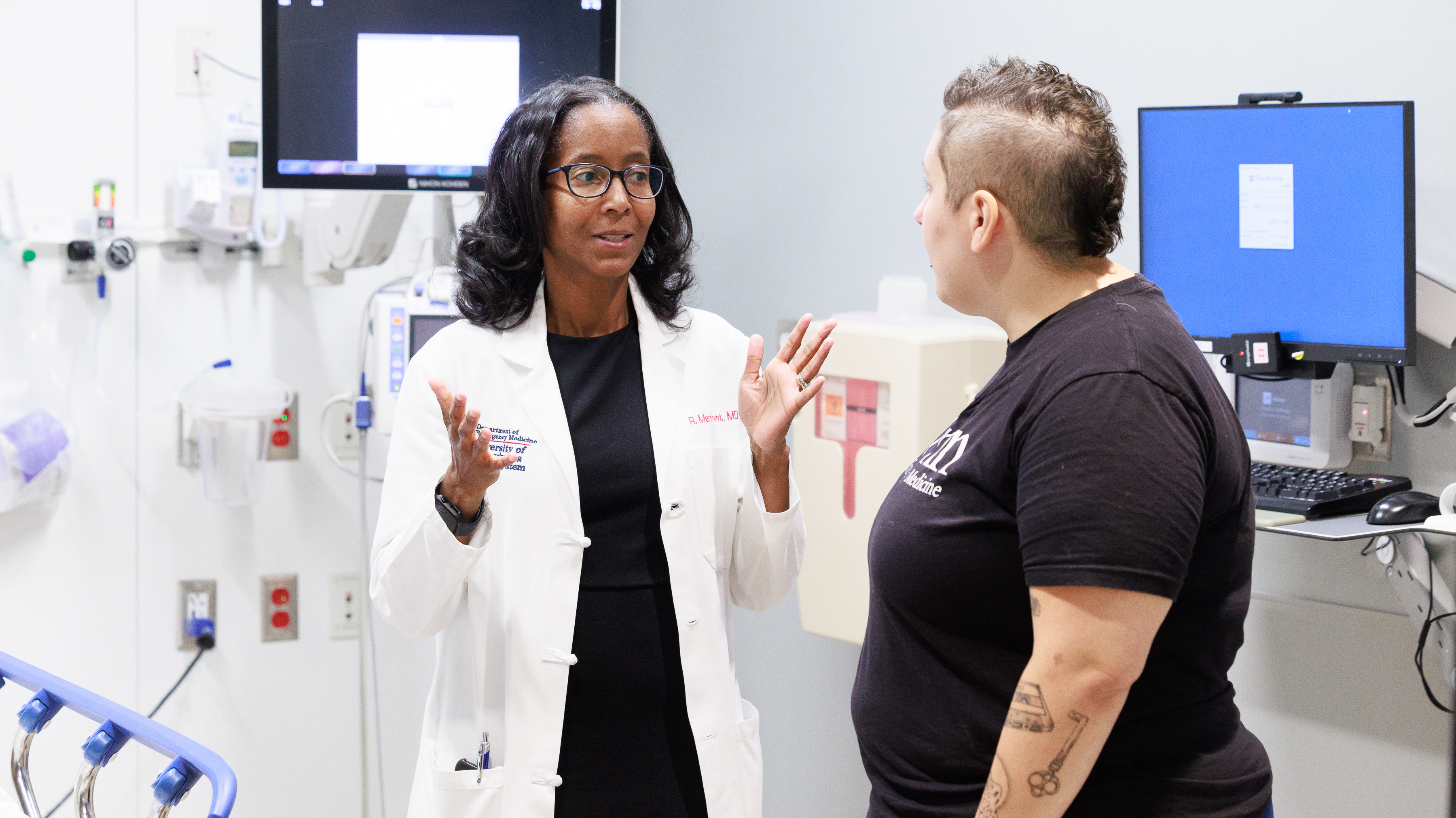  Raina Merchant, wearing a white coat, speaks with a staff member in the emergency department