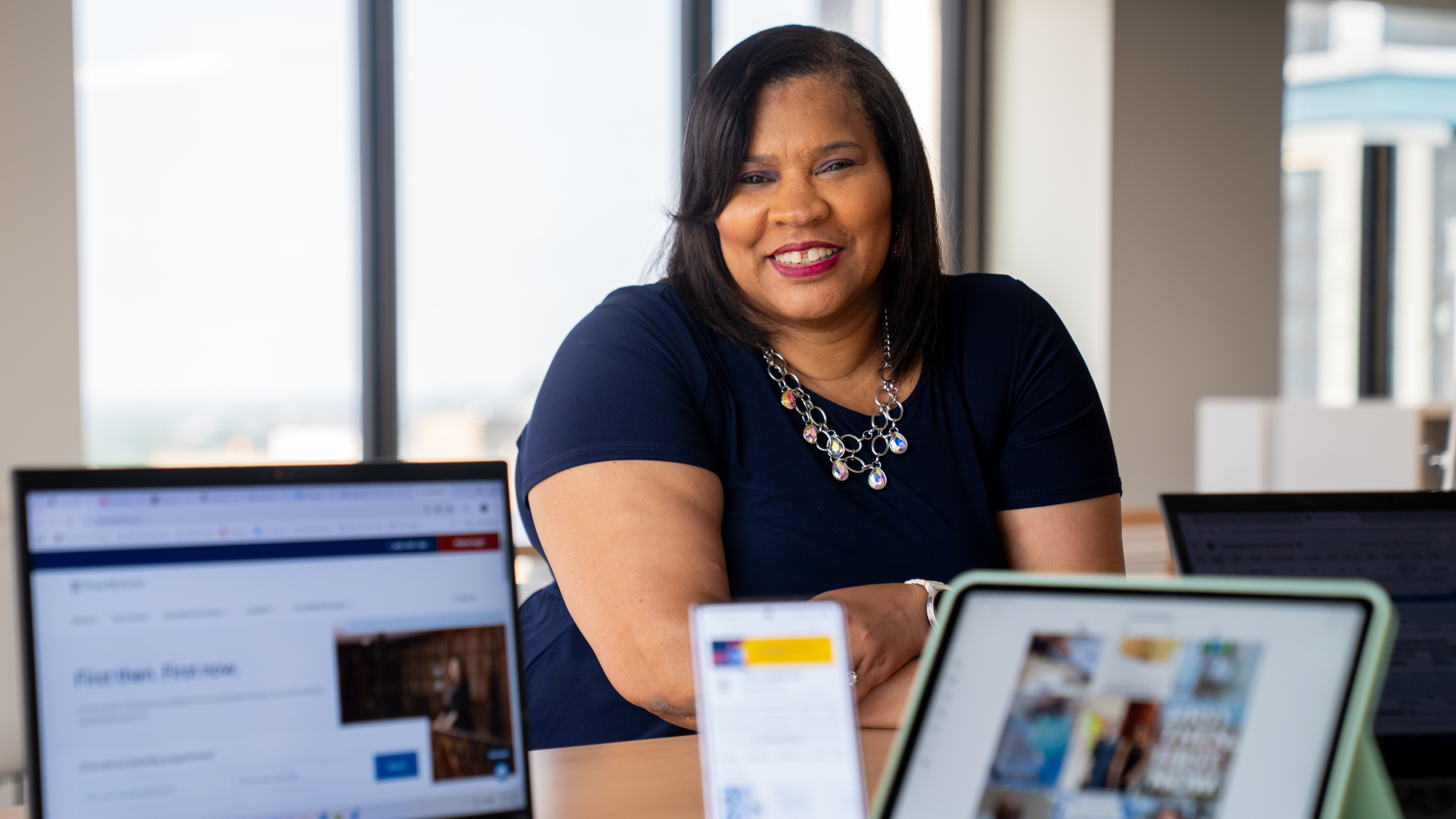 Deidre Gray at a desk with a laptop, phone, and tablet