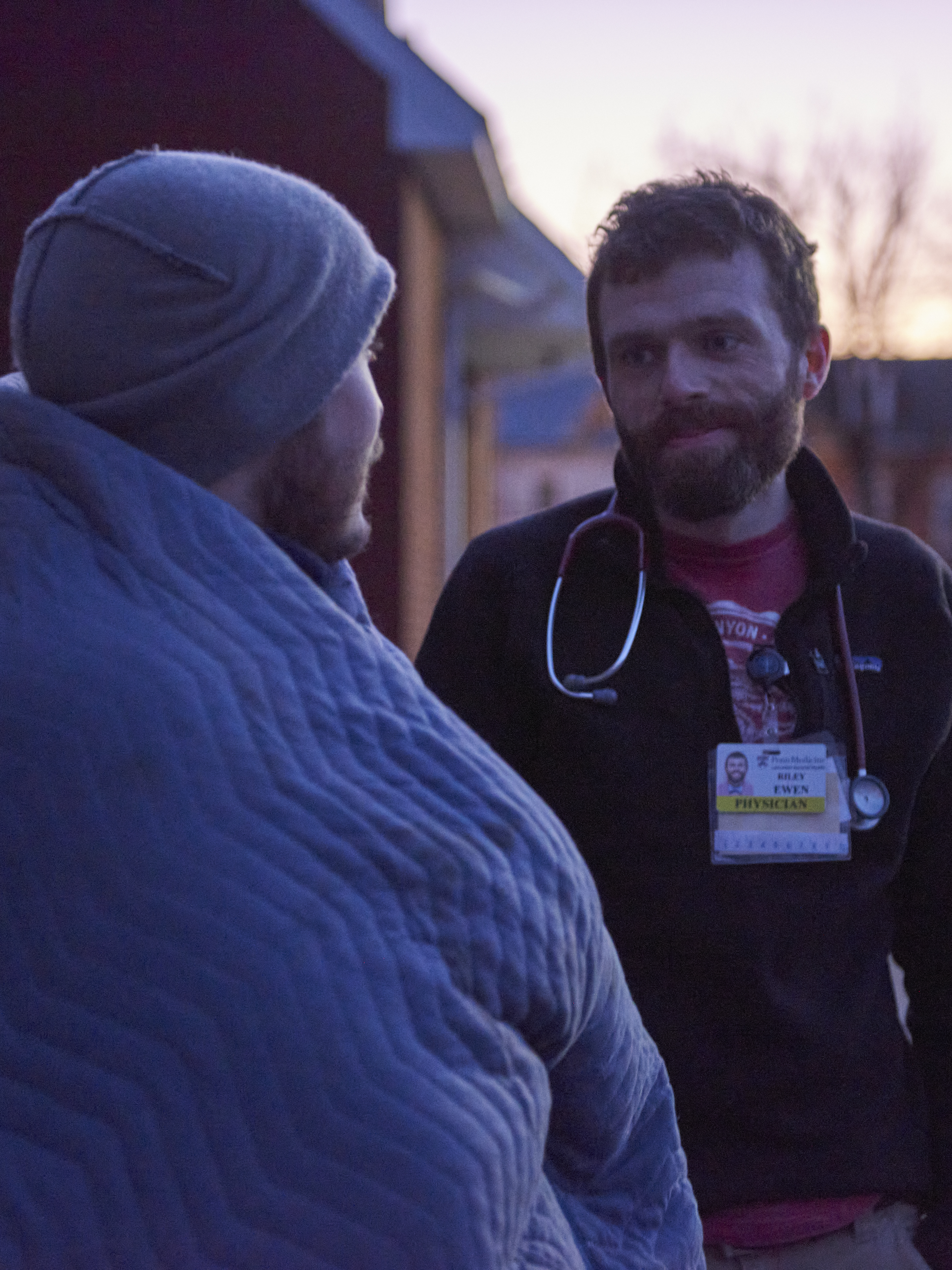 Dr. Riley Ewen speaks with a man wrapped in a blanket at twilight