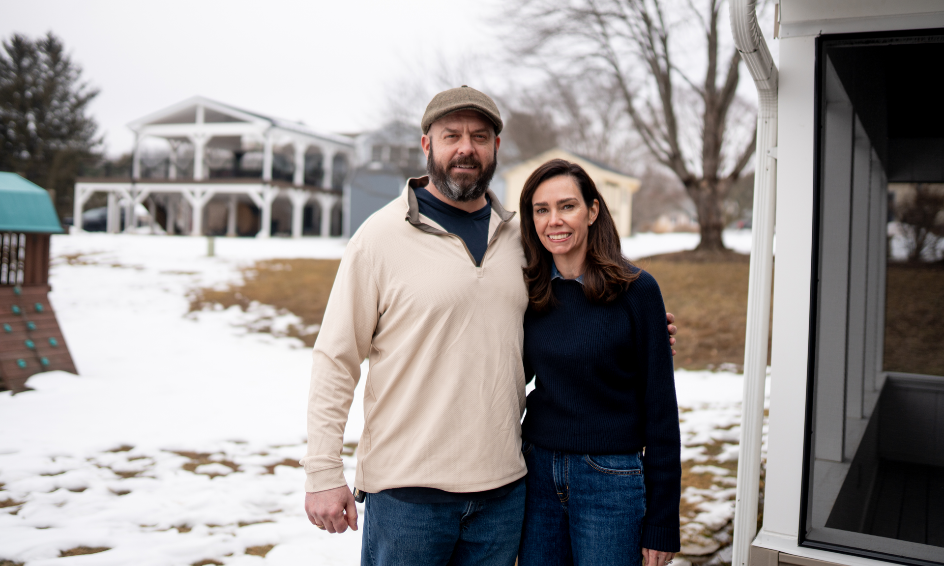 Dennis and Lauren Massimo in 2026, standing on the porch of Lauren's house, with Dennis' home in the background