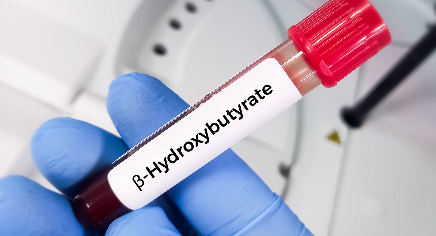 A gloved hand holding a vial of BHB