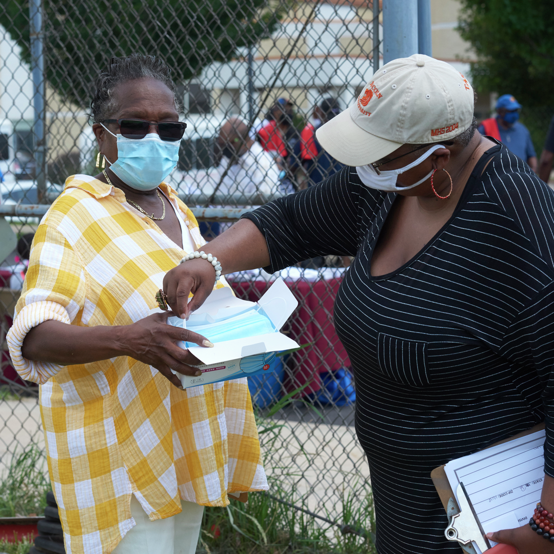 A Black woman holds a box of face masks to give out to attendees at an event
