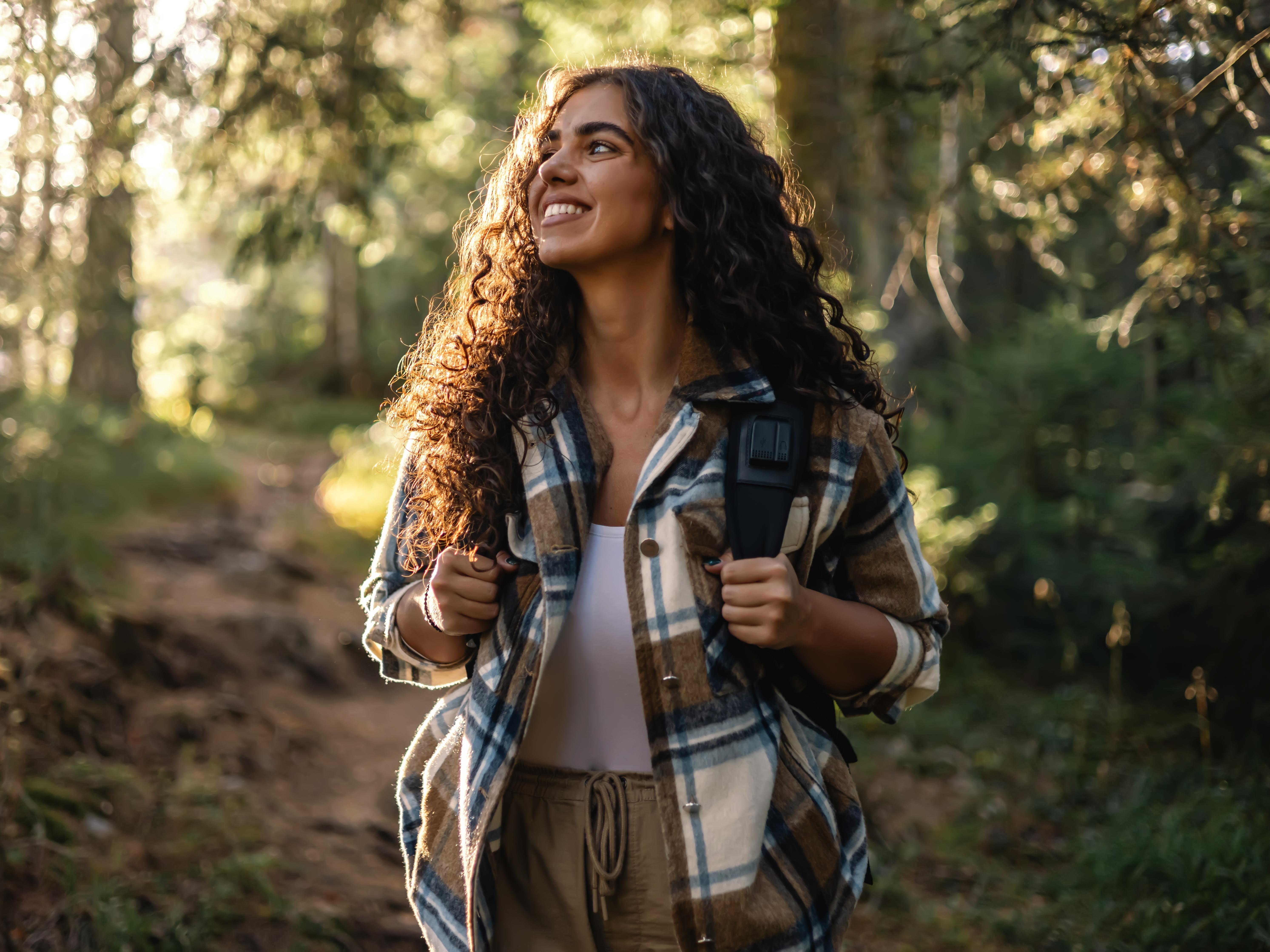 A young woman hiking alone on a forest path surrounded by trees.