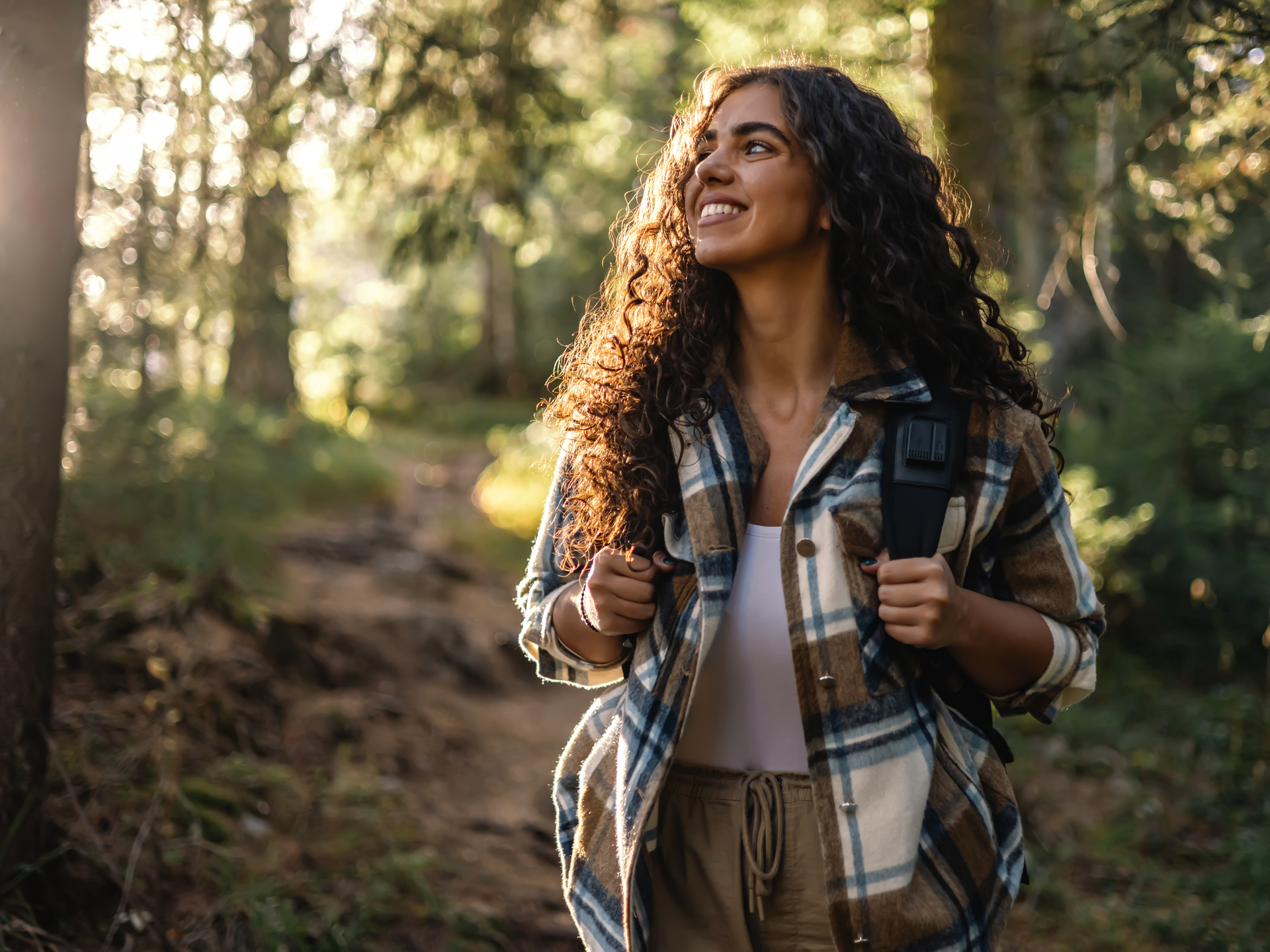 A young woman hiking alone on a forest path surrounded by trees.