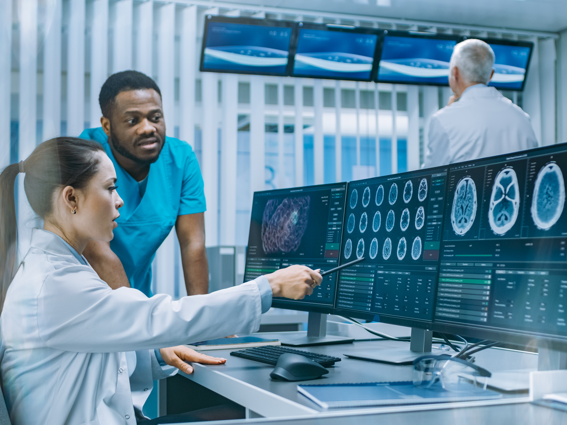 Medical scientist and surgeon discussing CT Brain scan images on computer screens.