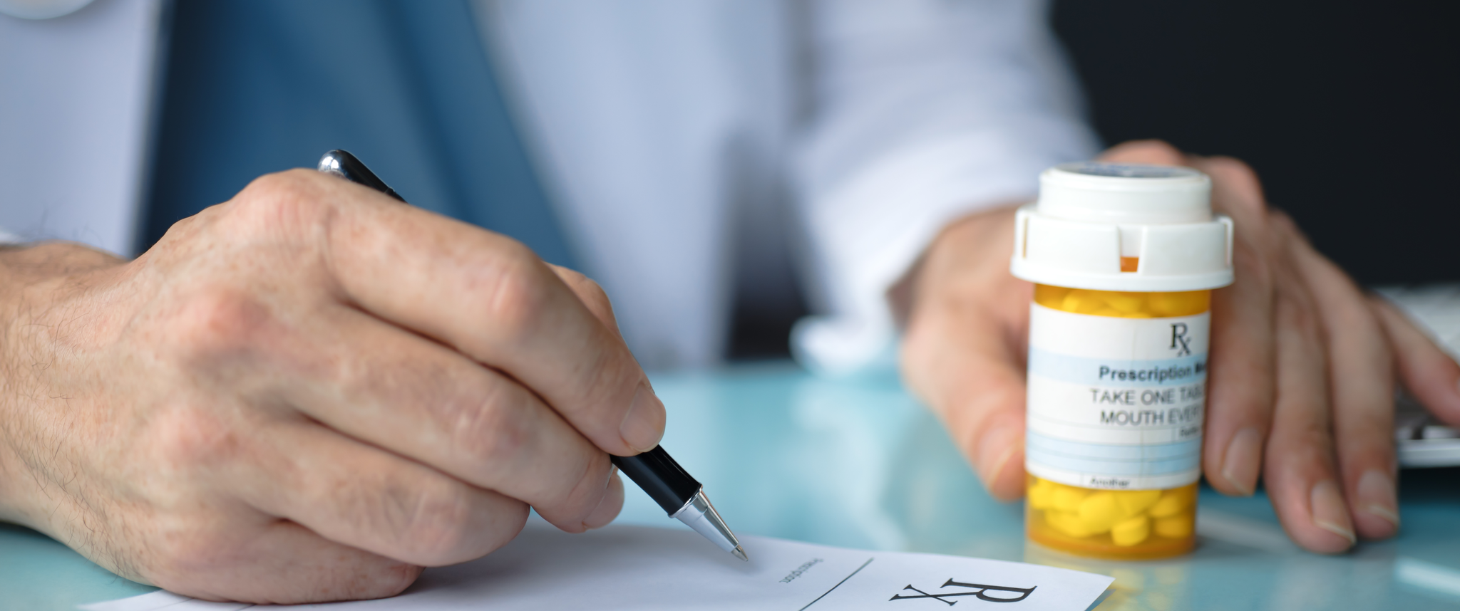 Doctor writing a prescription for medication with a bottle of pills next to them