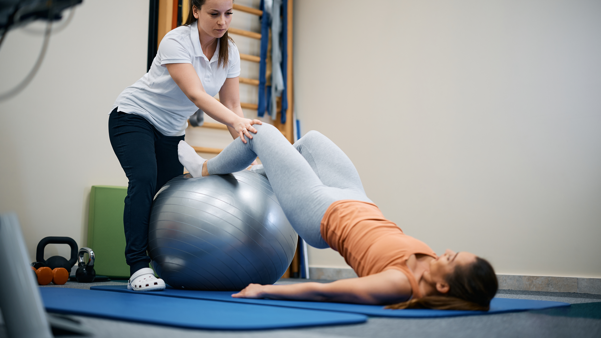 Female physiotherapist assisting young woman with physical therapy exercises