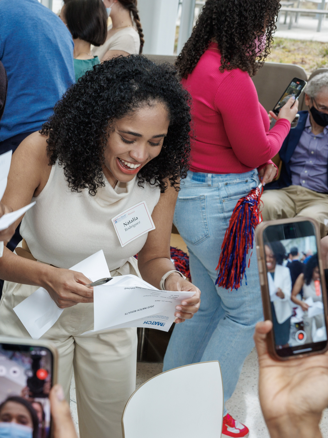 Canada Montgomery and Natalia Rodriguez stand side by side, looking at individual papers from their envelopes, with huge smiles reacting