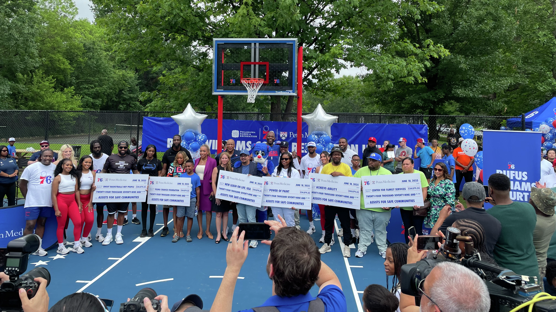 A group of people holding several large checks on a basketball court