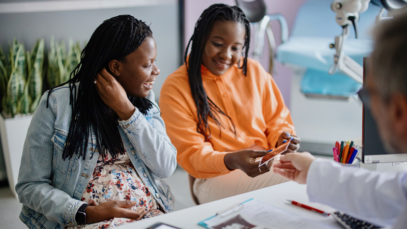 A pregnant woman and her wife smiling as a doctor hands them ultrasounds of their fetus