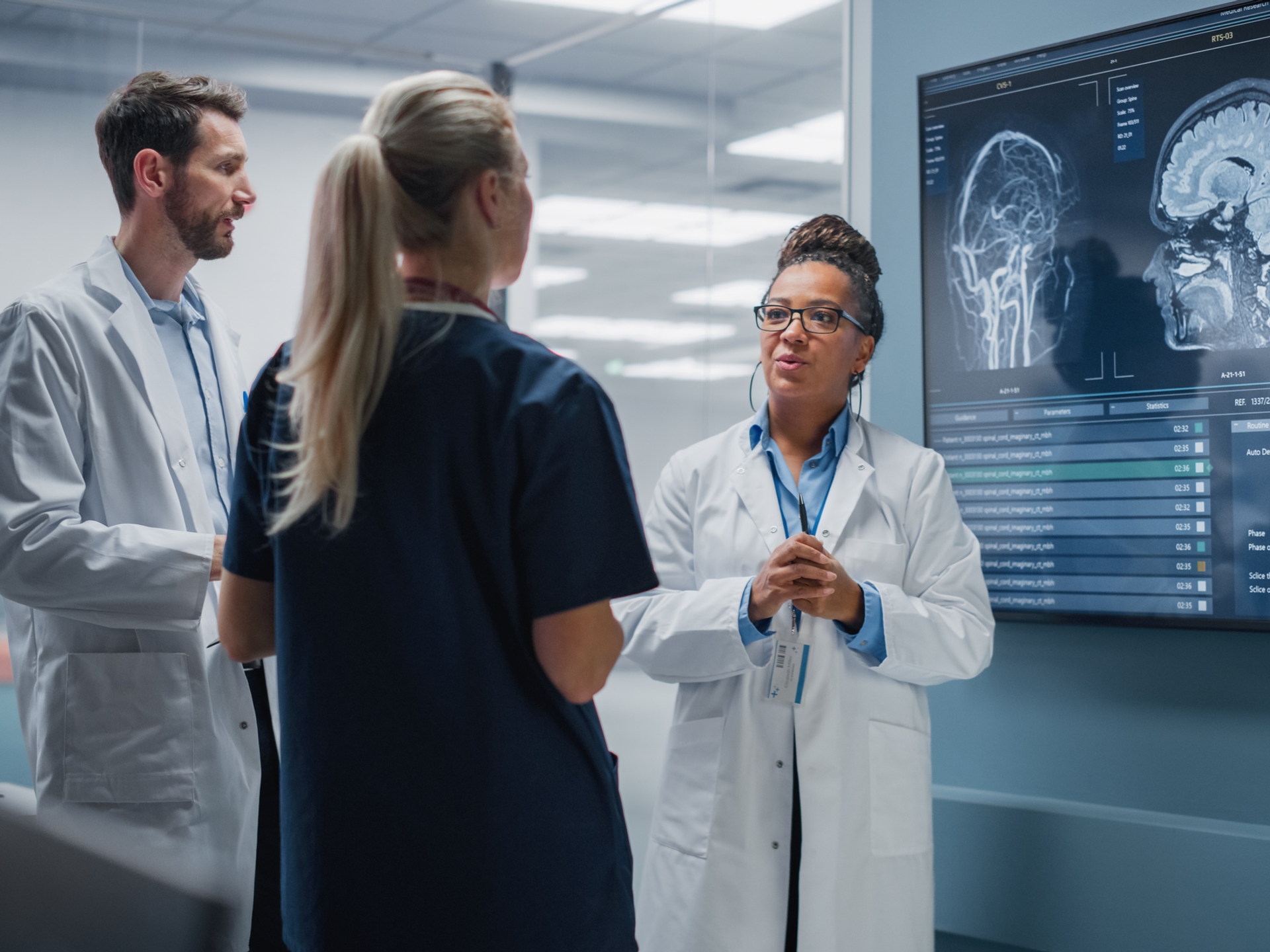 Medical Science Hospital Lab Meeting: Diverse Team of Neurologists, Neuroscientists, Neurosurgeon Consult TV Screen Showing MRI Scan with Brain Images