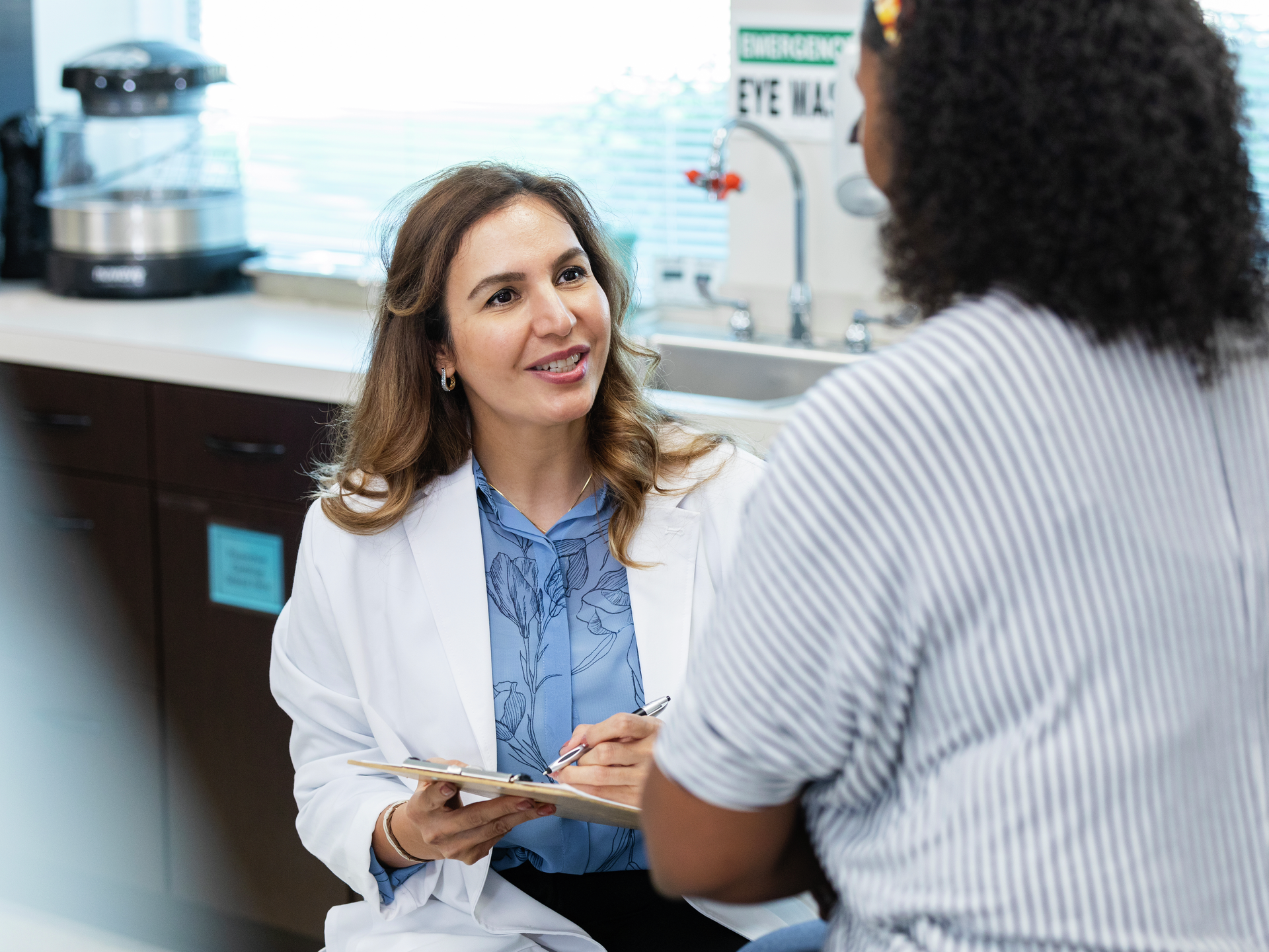 Unrecognizable female patient answers questions while doctor writes information in medical chart.