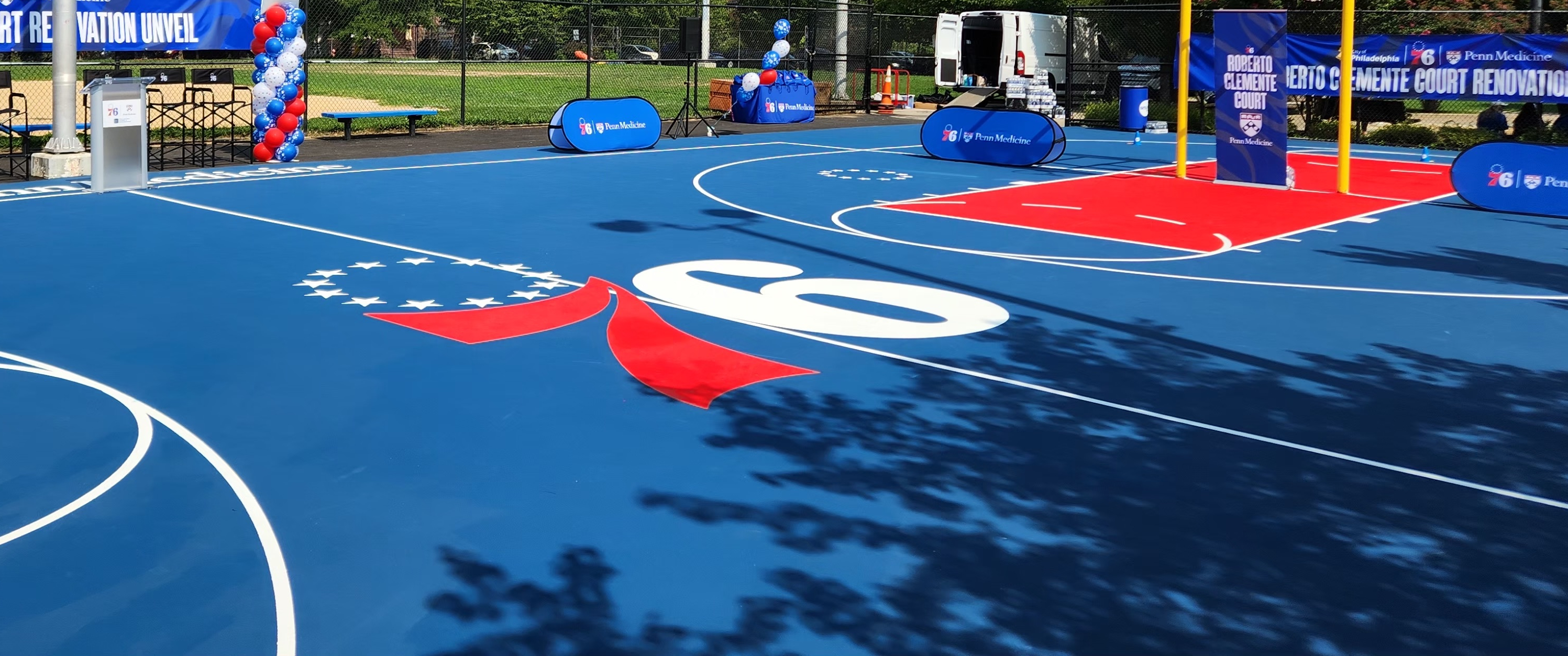 A large, clean community basketball court with 76ers logo at center