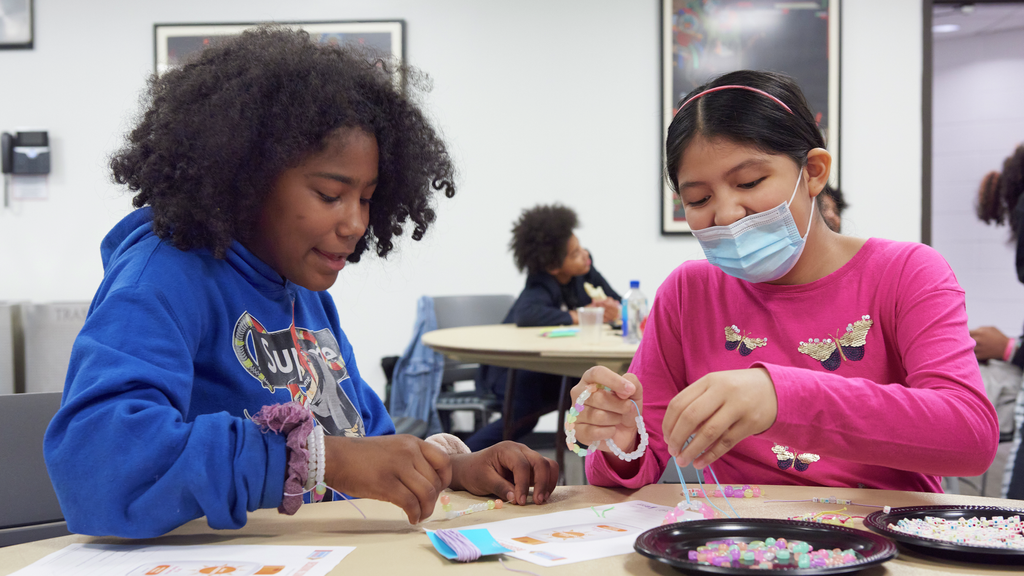 Two middle school-aged girls make beaded bracelets