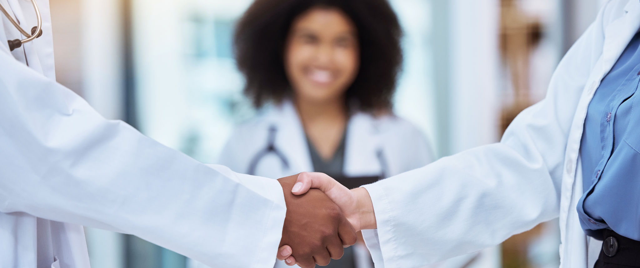 Doctors shake each other's hands while another doctor smiles in the background