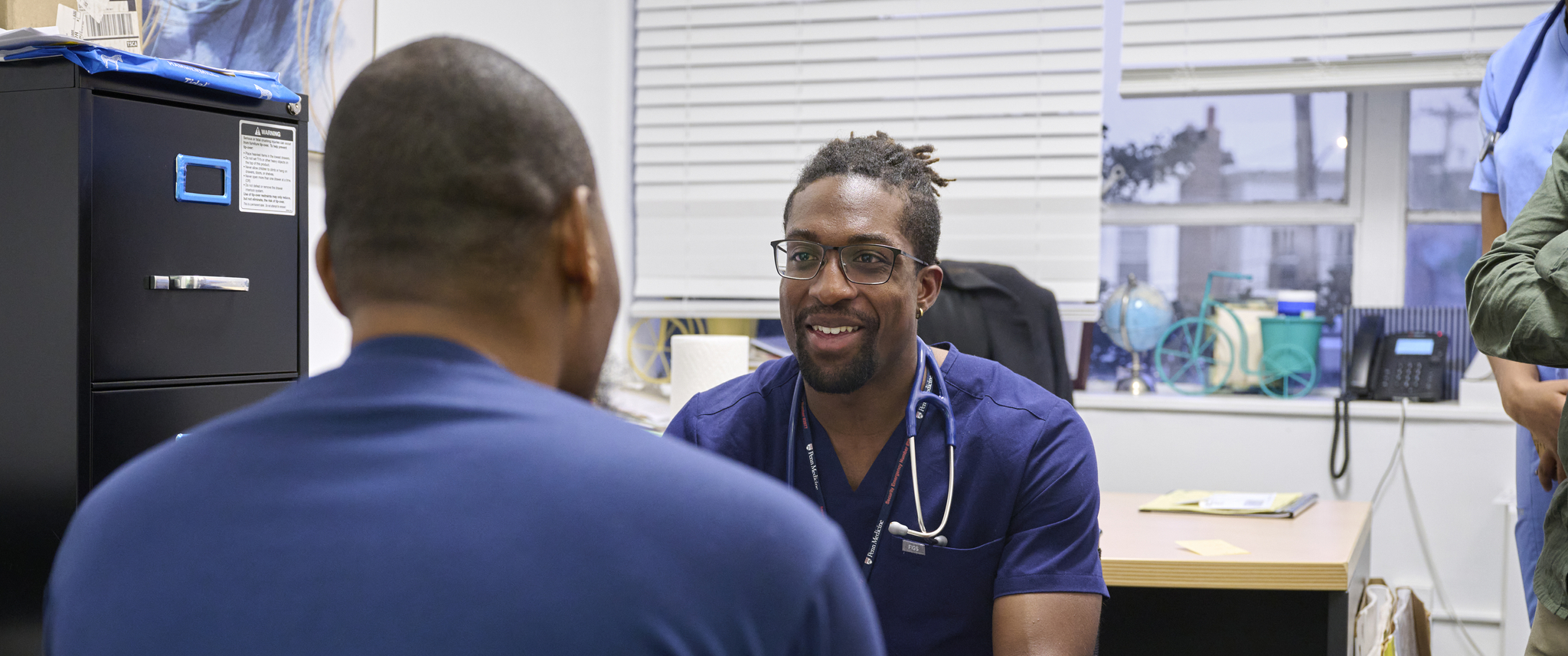 A Penn Medicine staff member in scrubs talks with a patient at the African Health Clinic