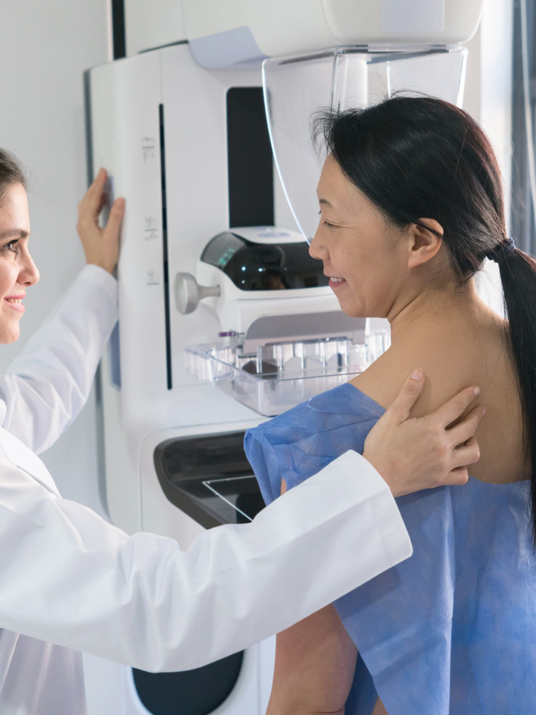 Female gynecologist helping a patient get in position for a mammogram 