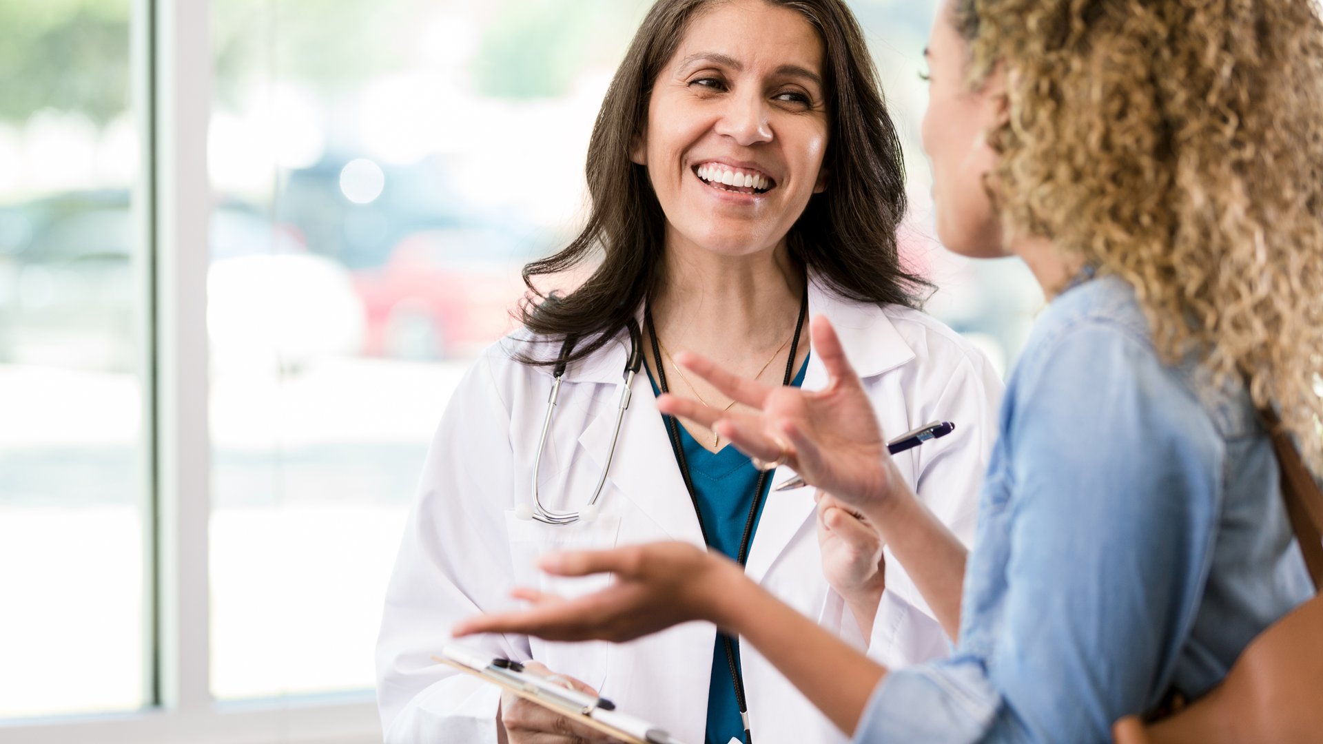 Female doctor smiles while listening to a female patient 