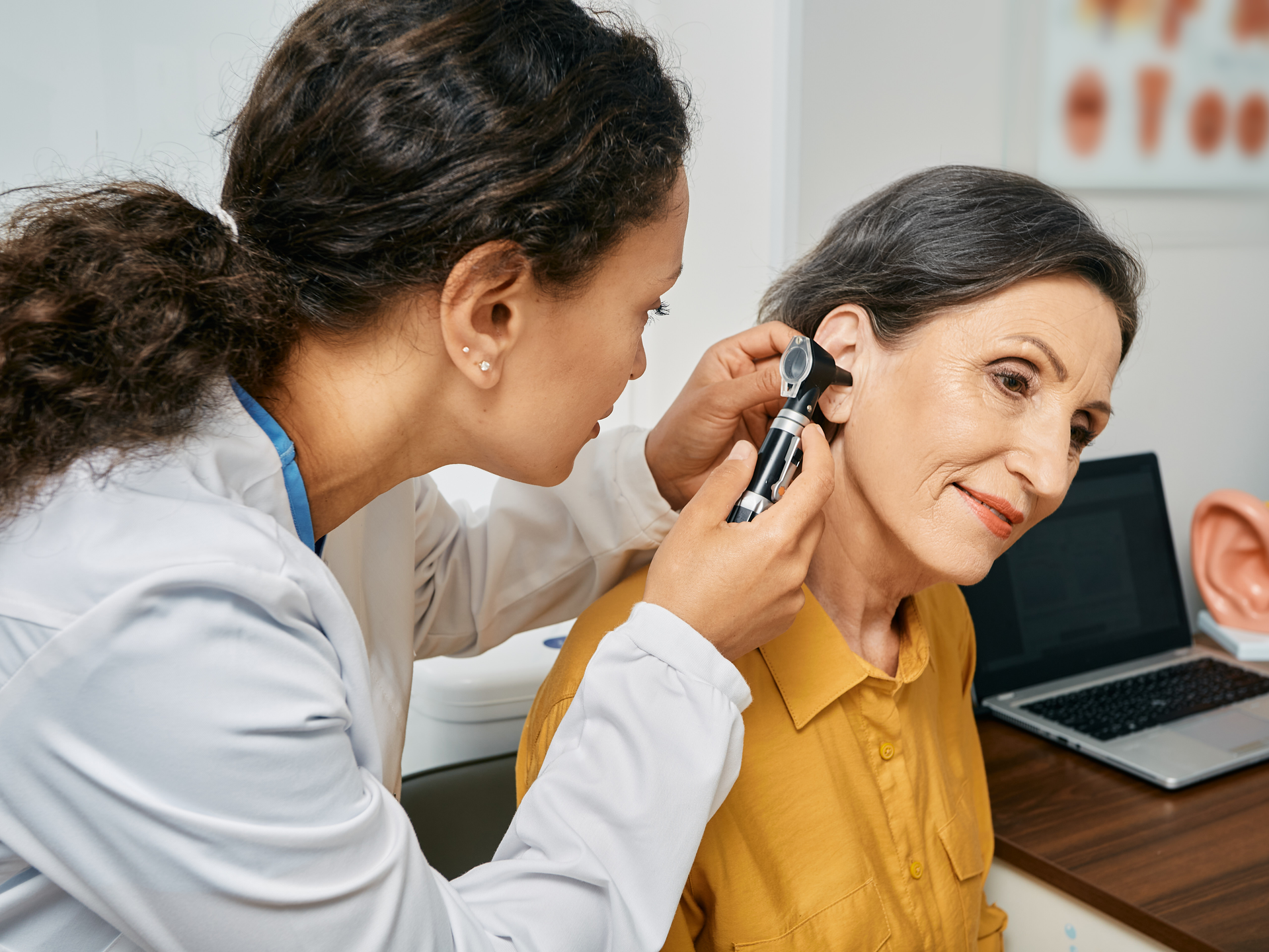 Otolaryngologist doctor checking mature woman's ear using otoscope or auriscope at medical clinic