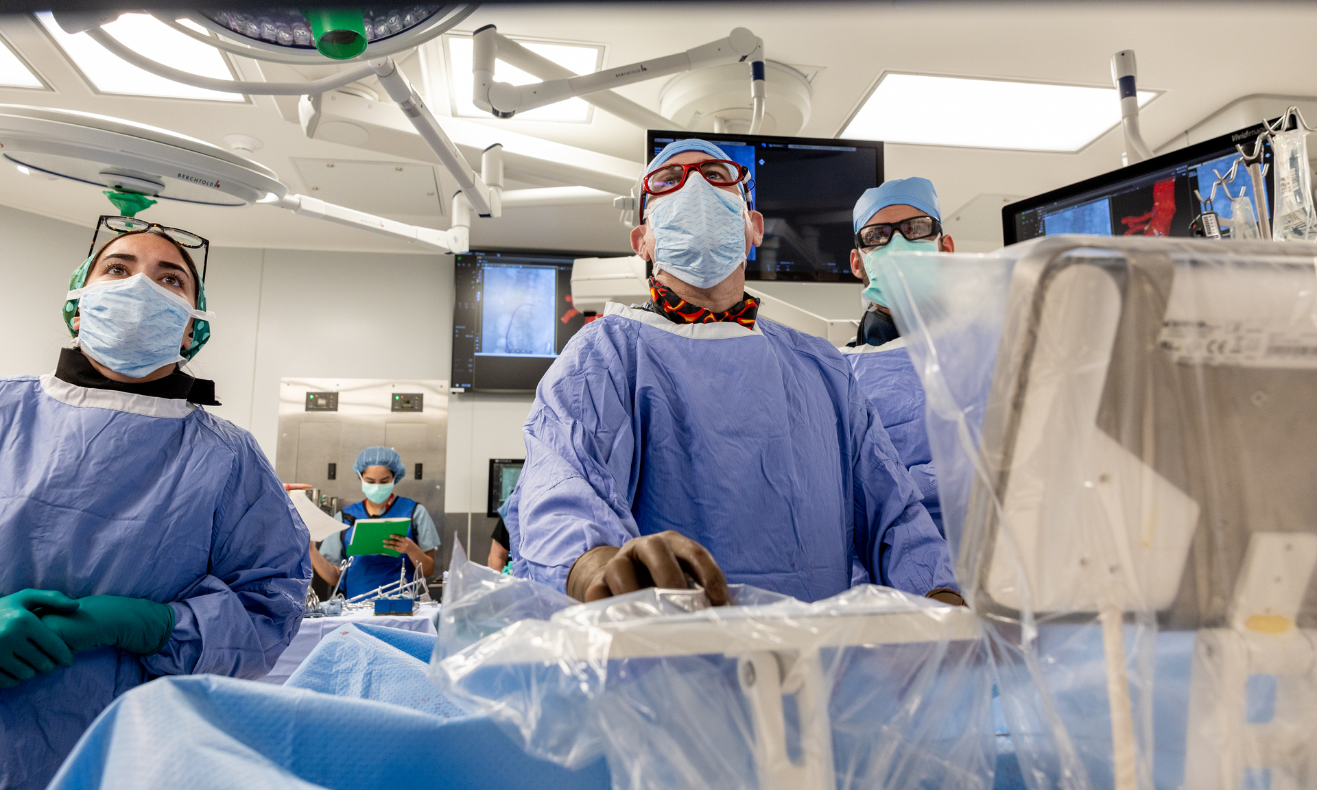 Three people wearing gowns, masks, and surgical bonnets look up