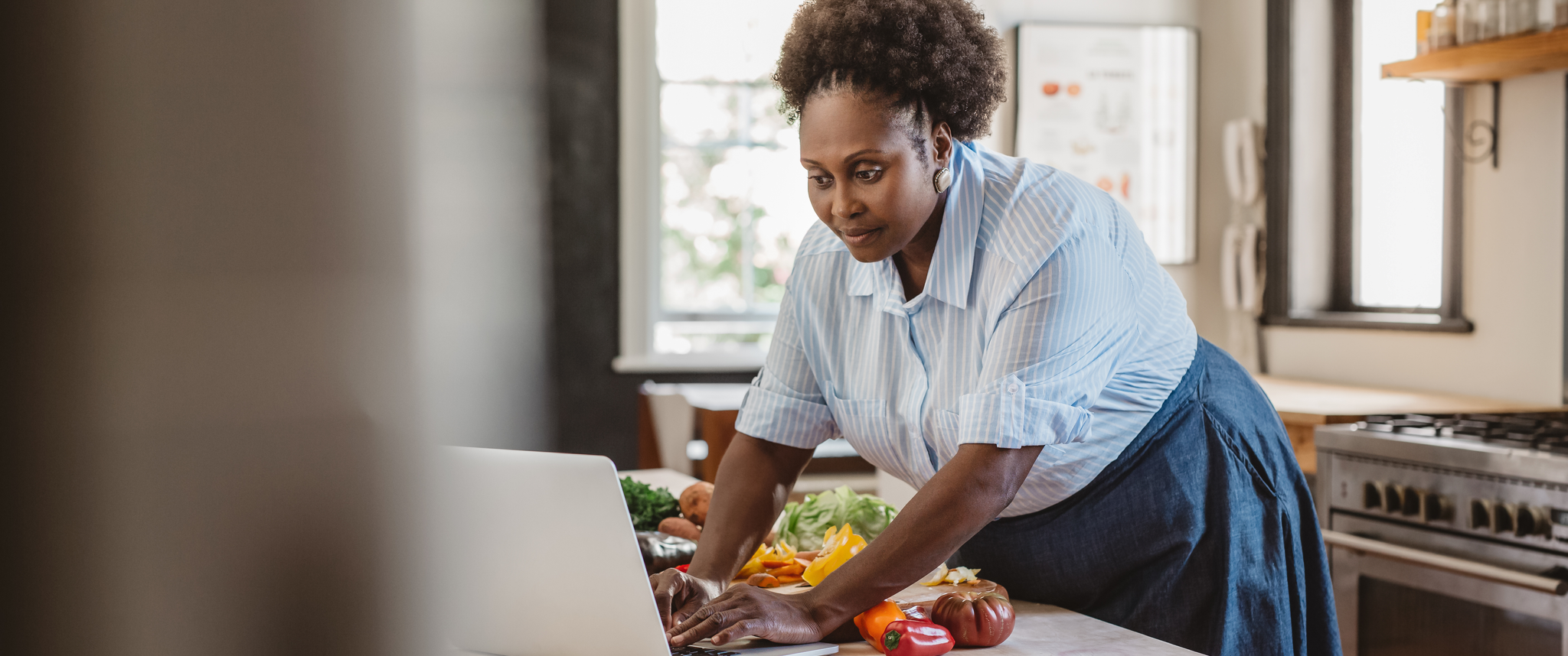 Black woman at kitchen table with computer and vegtables