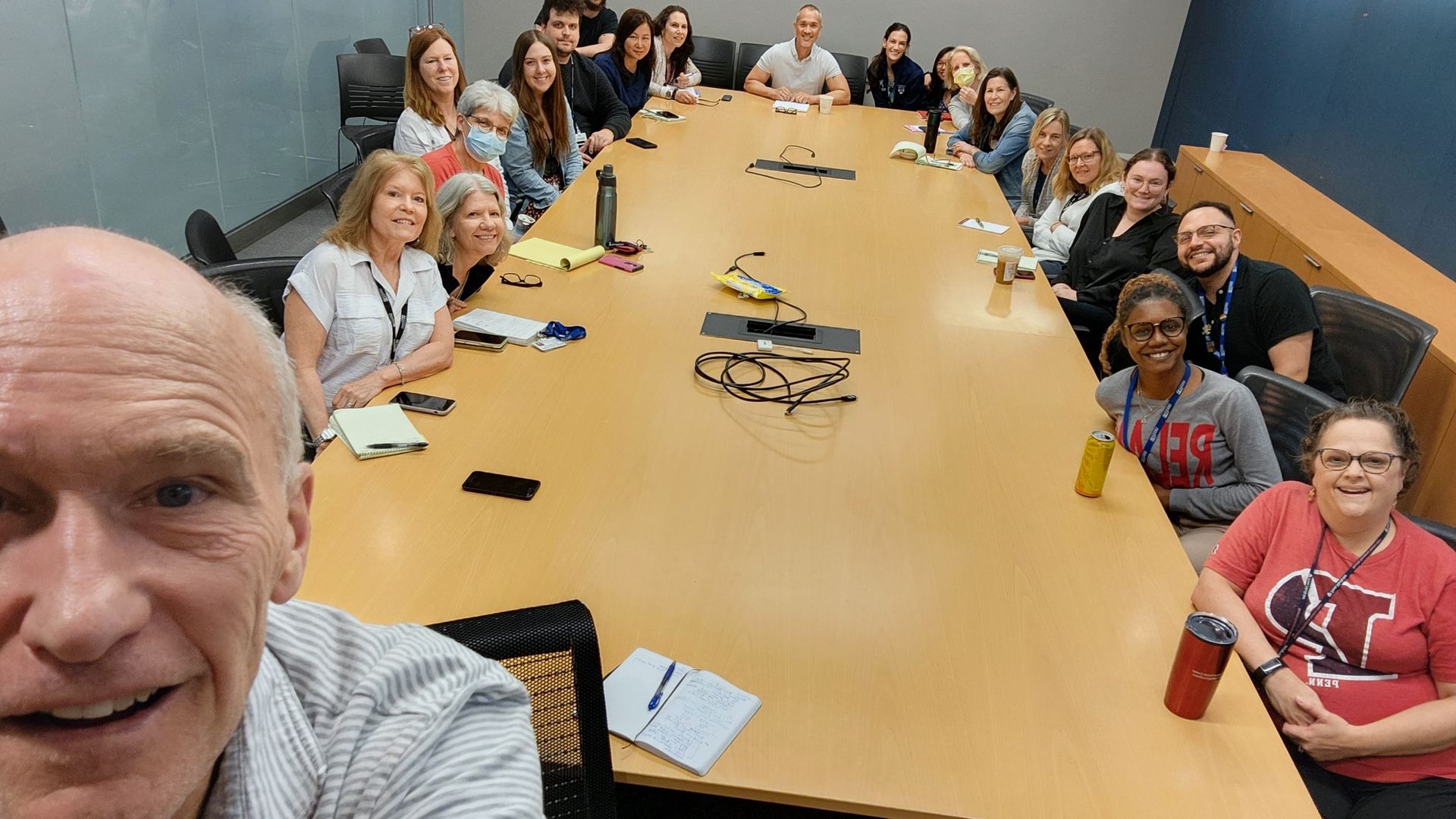 A group selfie taken by Carl June in the foreground with CTU staff arrayed around a conference table behind him, smiling