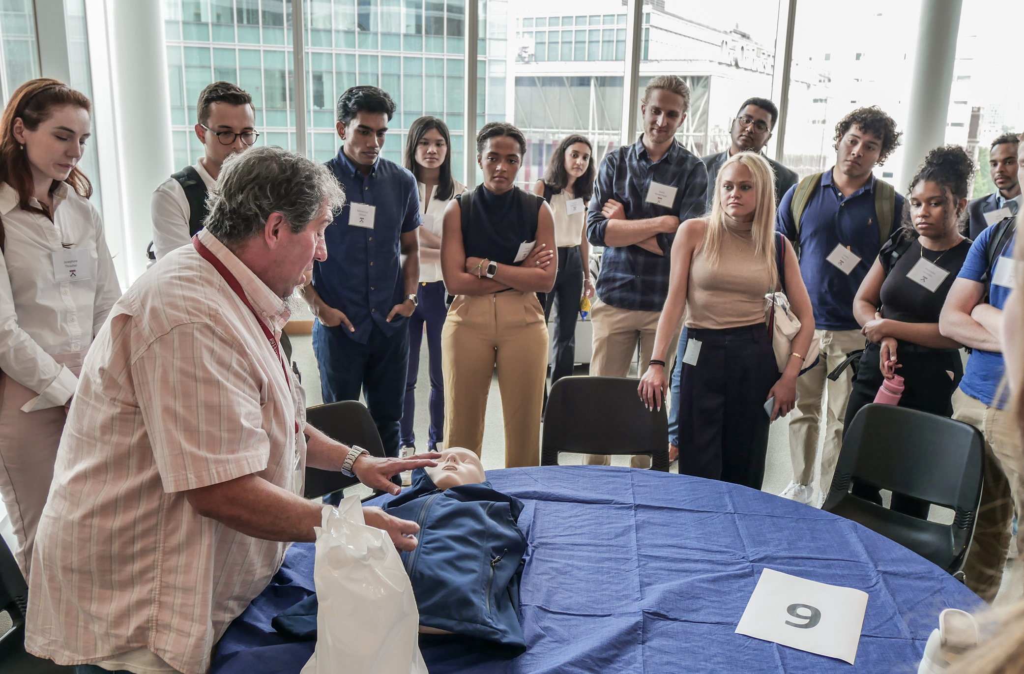 A group of medical students gathers around a table where an instructor is pointing to a manikin 