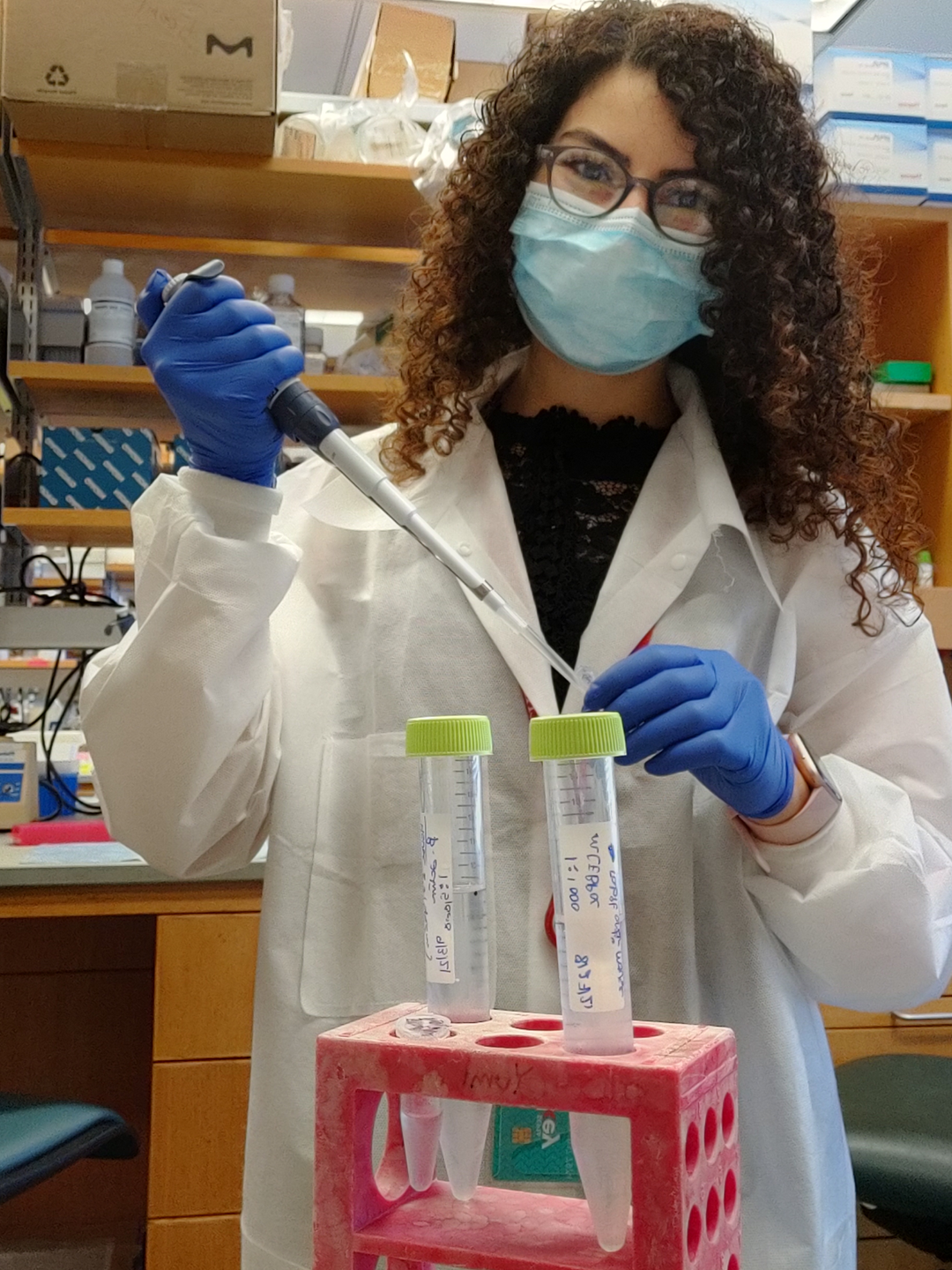 Mayassa Bou-Dargham, wearing a lab coat and mask, and holding a pipette