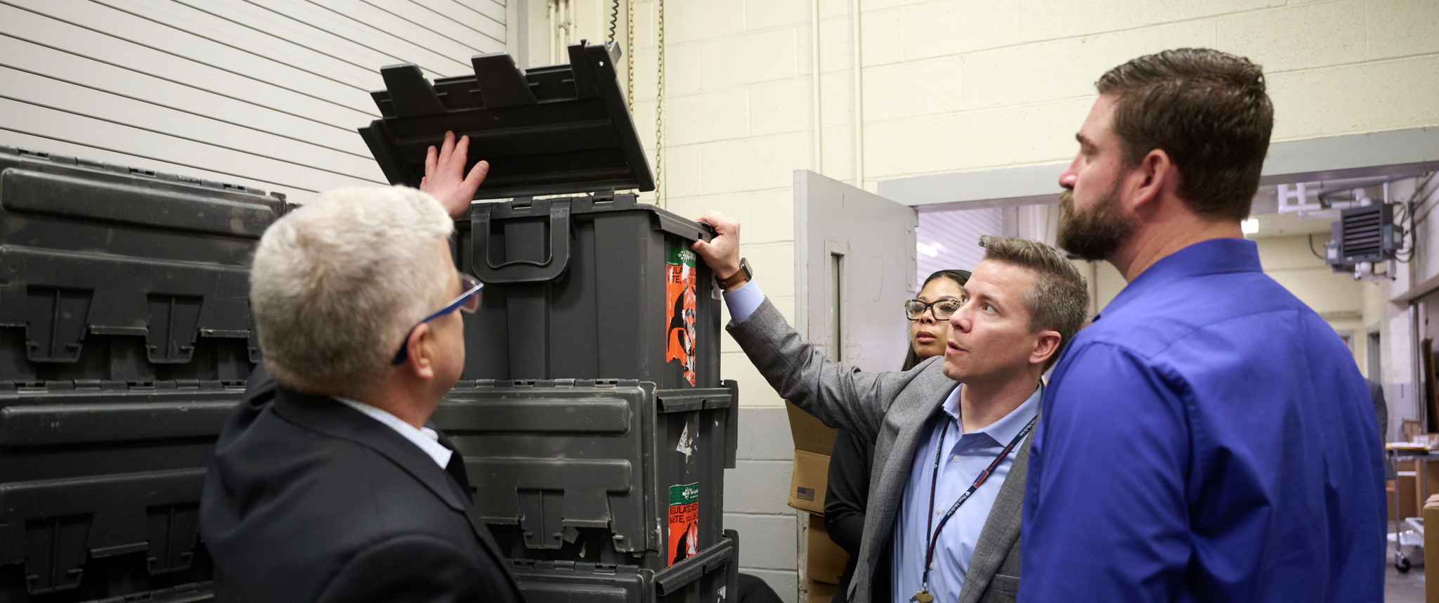 A group of three people gathers around looking at a stack of empty bins labeled “regulated medical waste.”