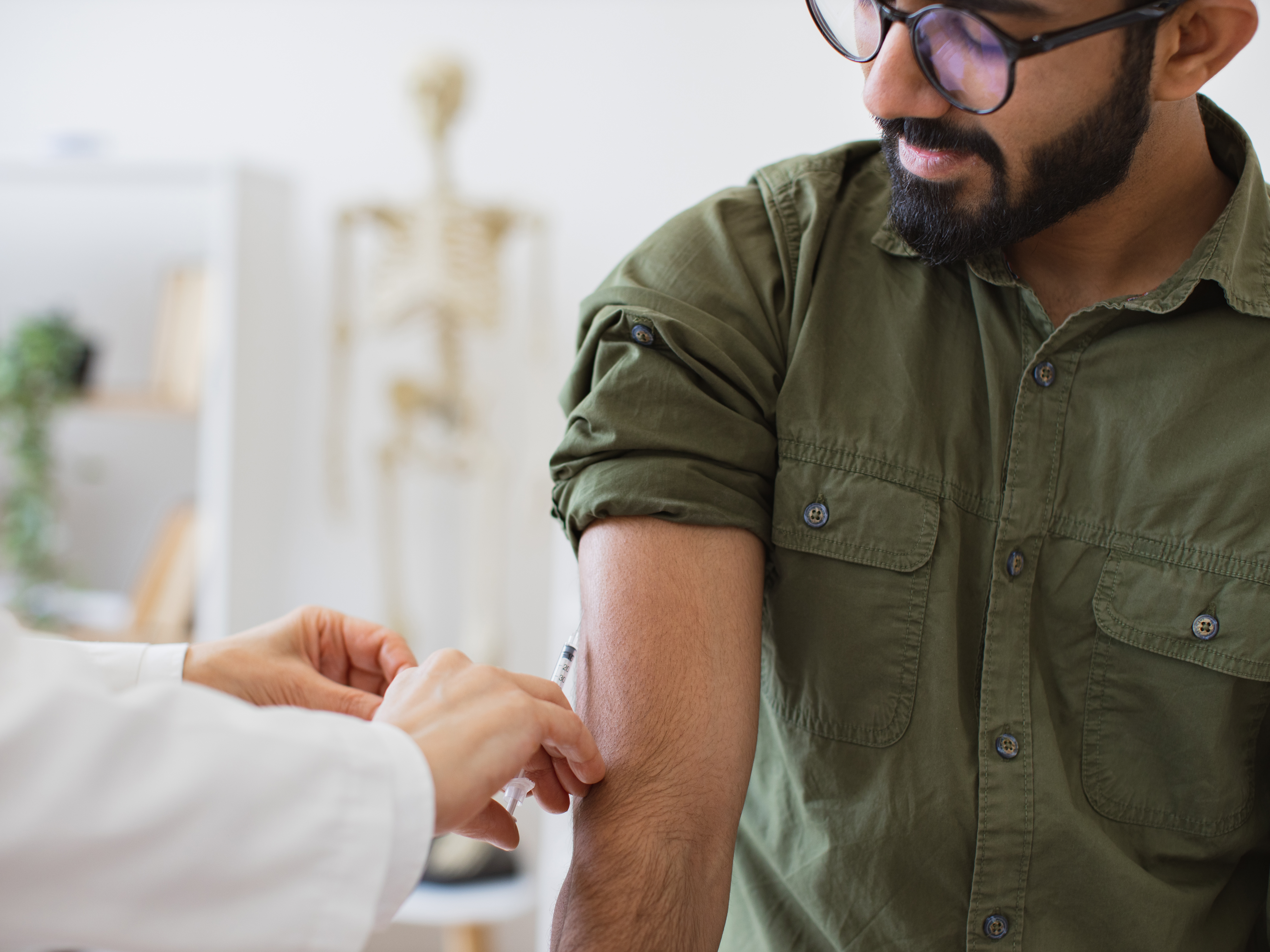 Doctor in lab coat holding syringe with seasonal flu vaccine while young man sitting in exam room.