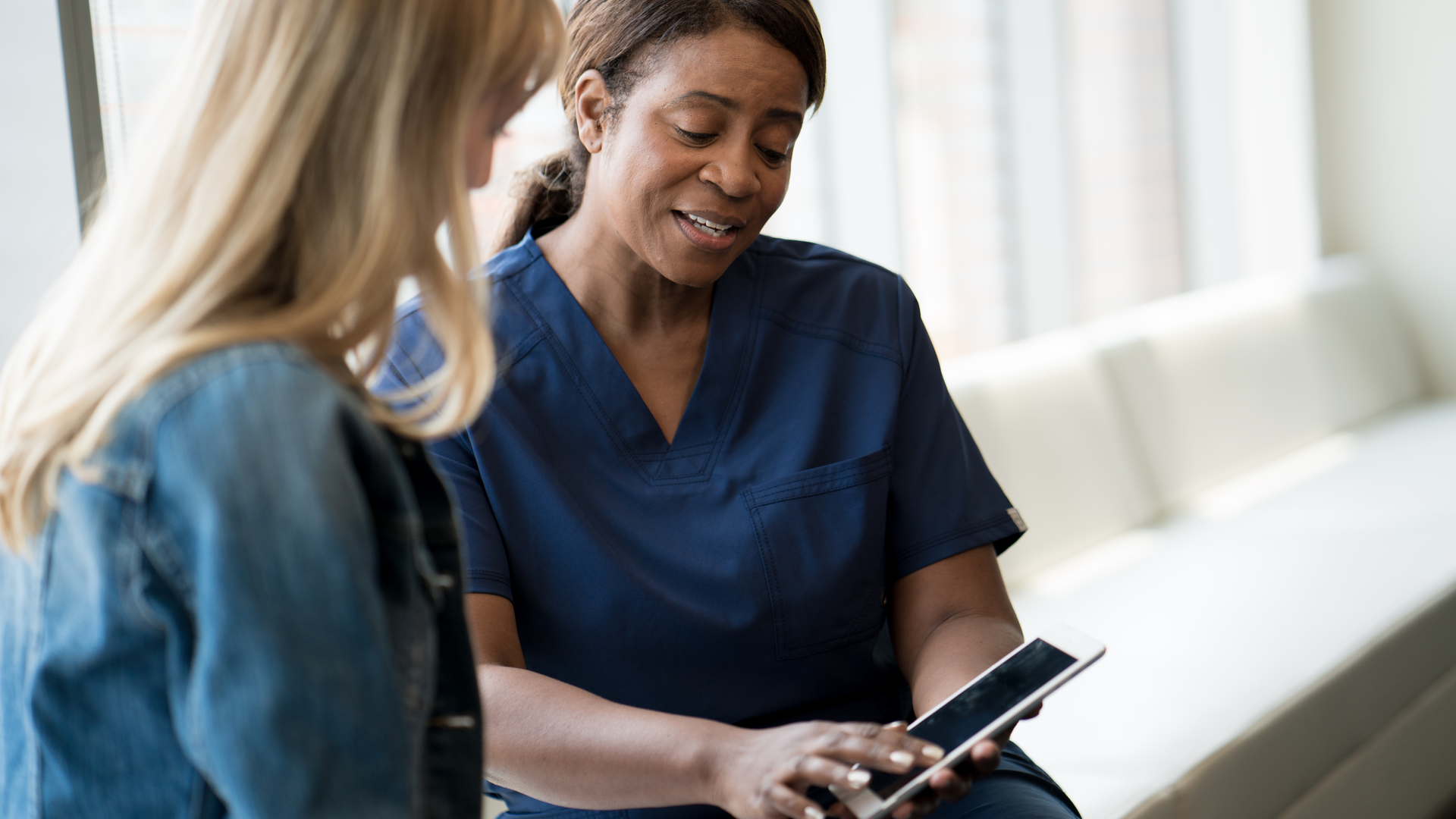 Primary care nurse talking to patient while pointing to tablet