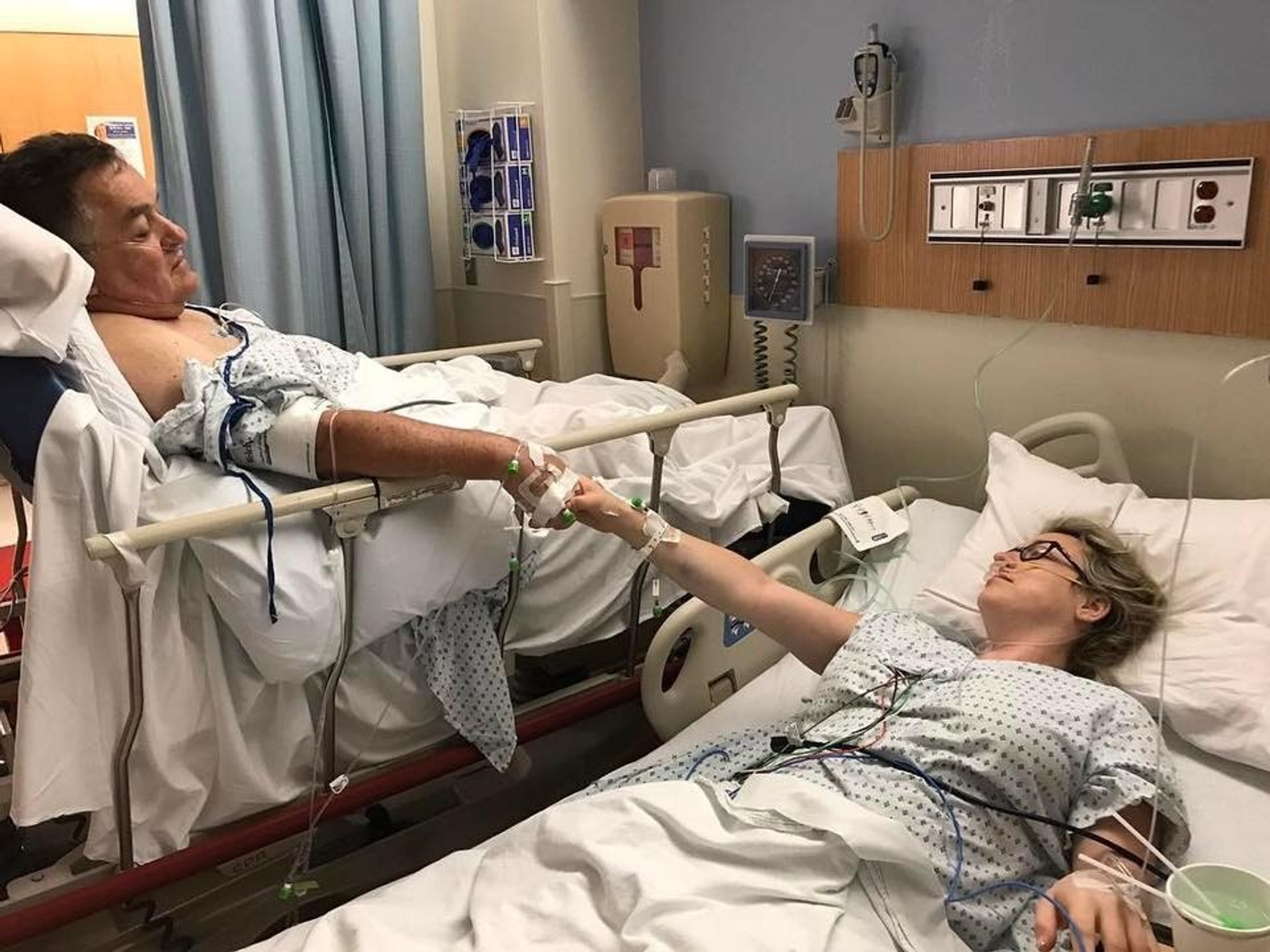Father and daughter reach for each other in their hospital beds before living donor kidney transplant surgery