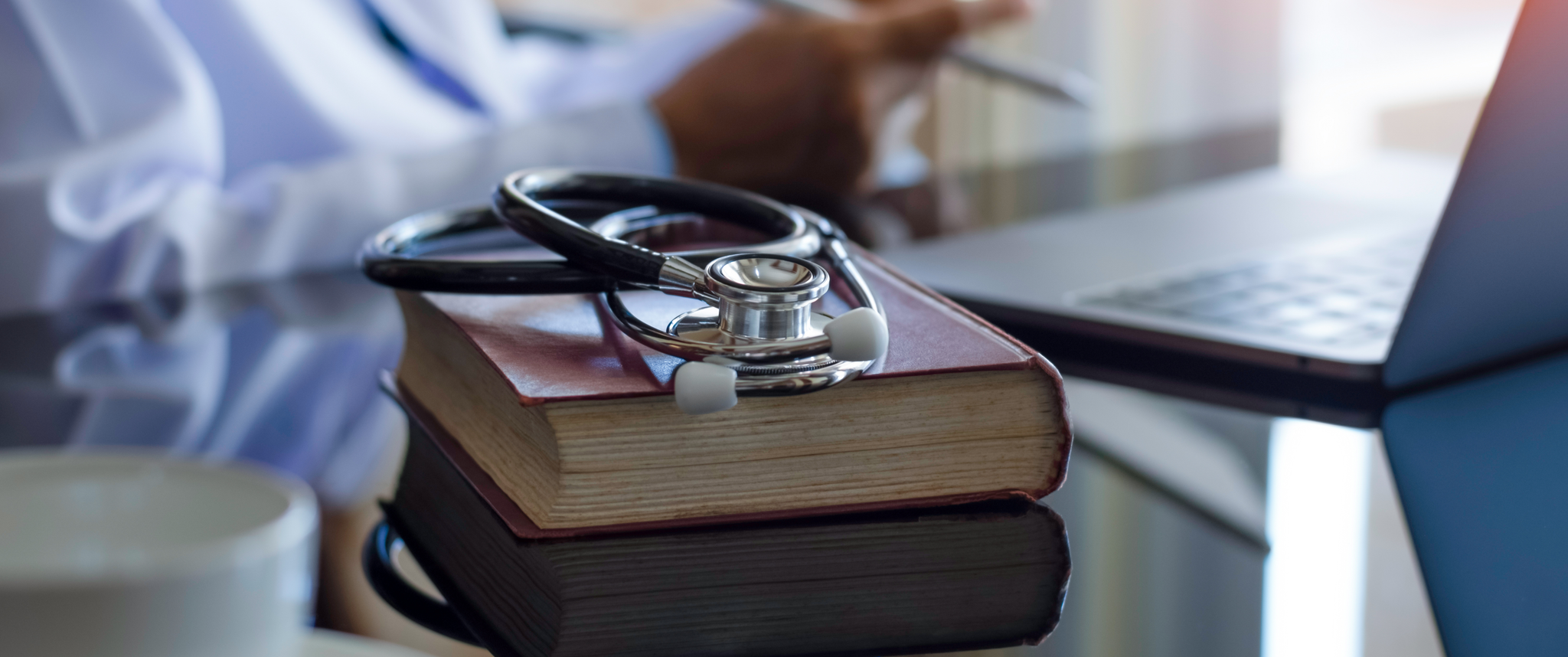 Doctor holding clipboard with laptop, teacup, books and stethoscope on office desk