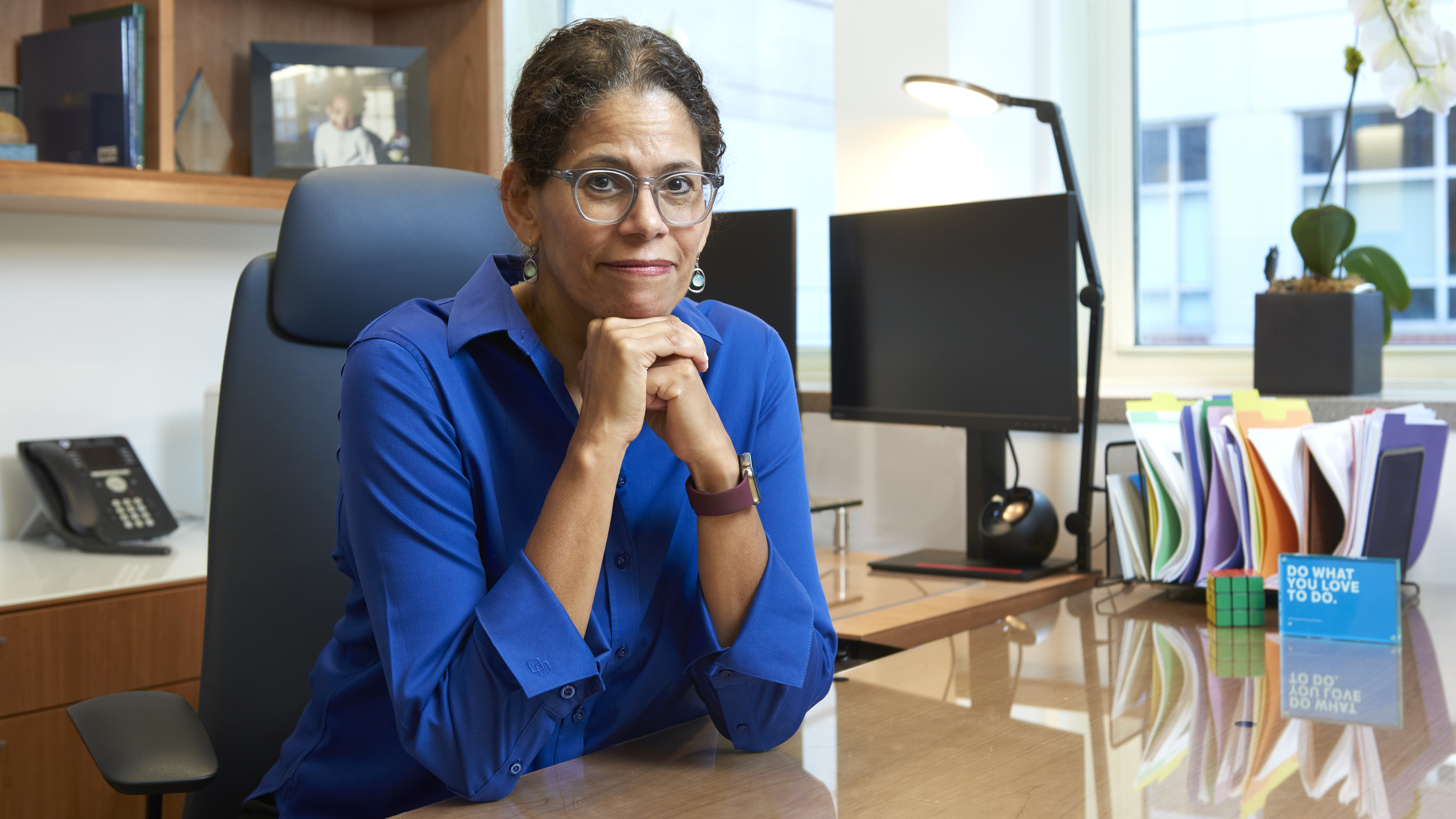 Elizabeth Howell, MD, seated at her desk looking directly at the viewer with a slight smile, her head leaning on her hands