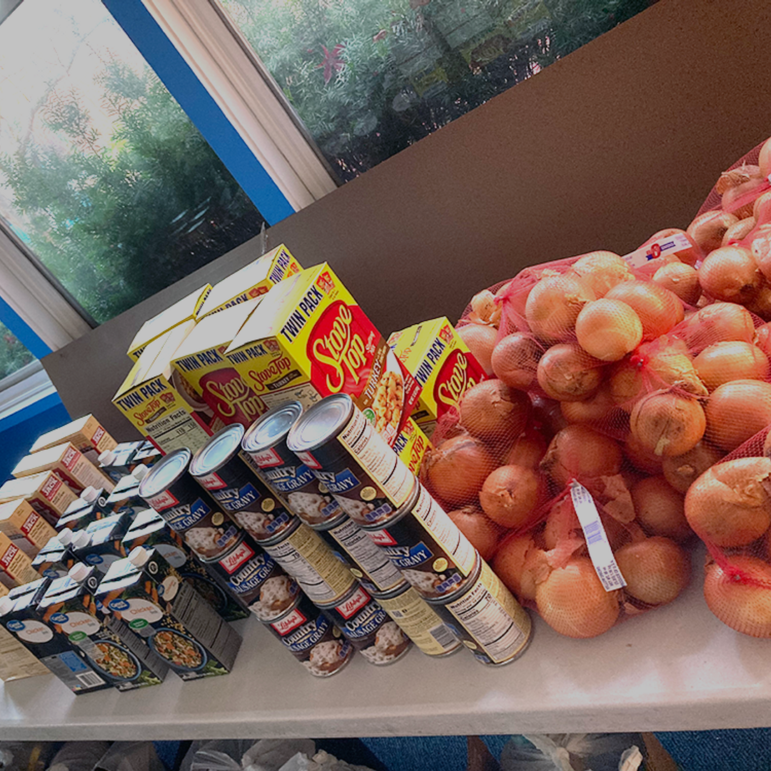 A countertop covered with canned and boxed food and onions