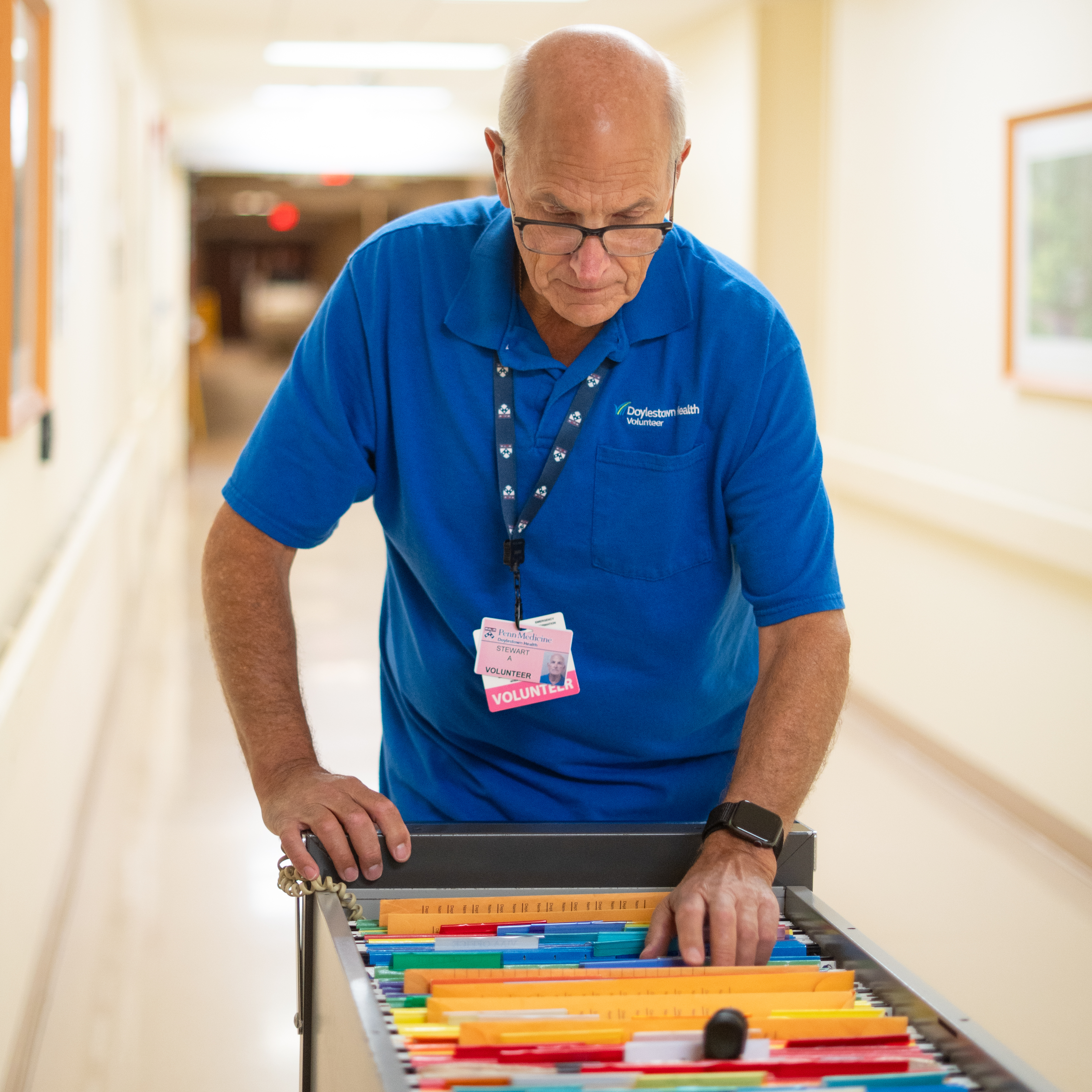 Stuart Avart, interoffice mail delivery volunteer, pushing a cart full of mail down a hospital hallway