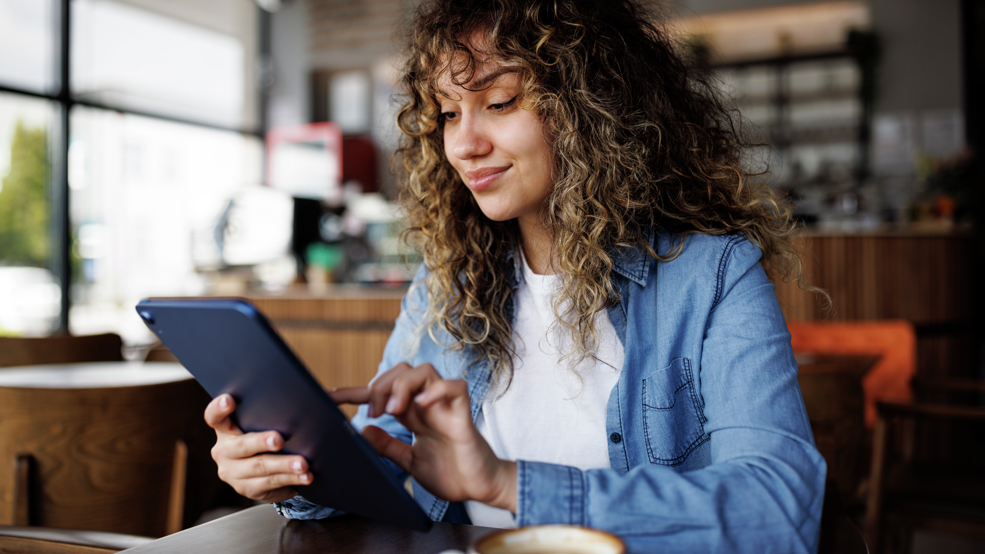 Young smiling woman using digital tablet and enjoying coffee at a cafe